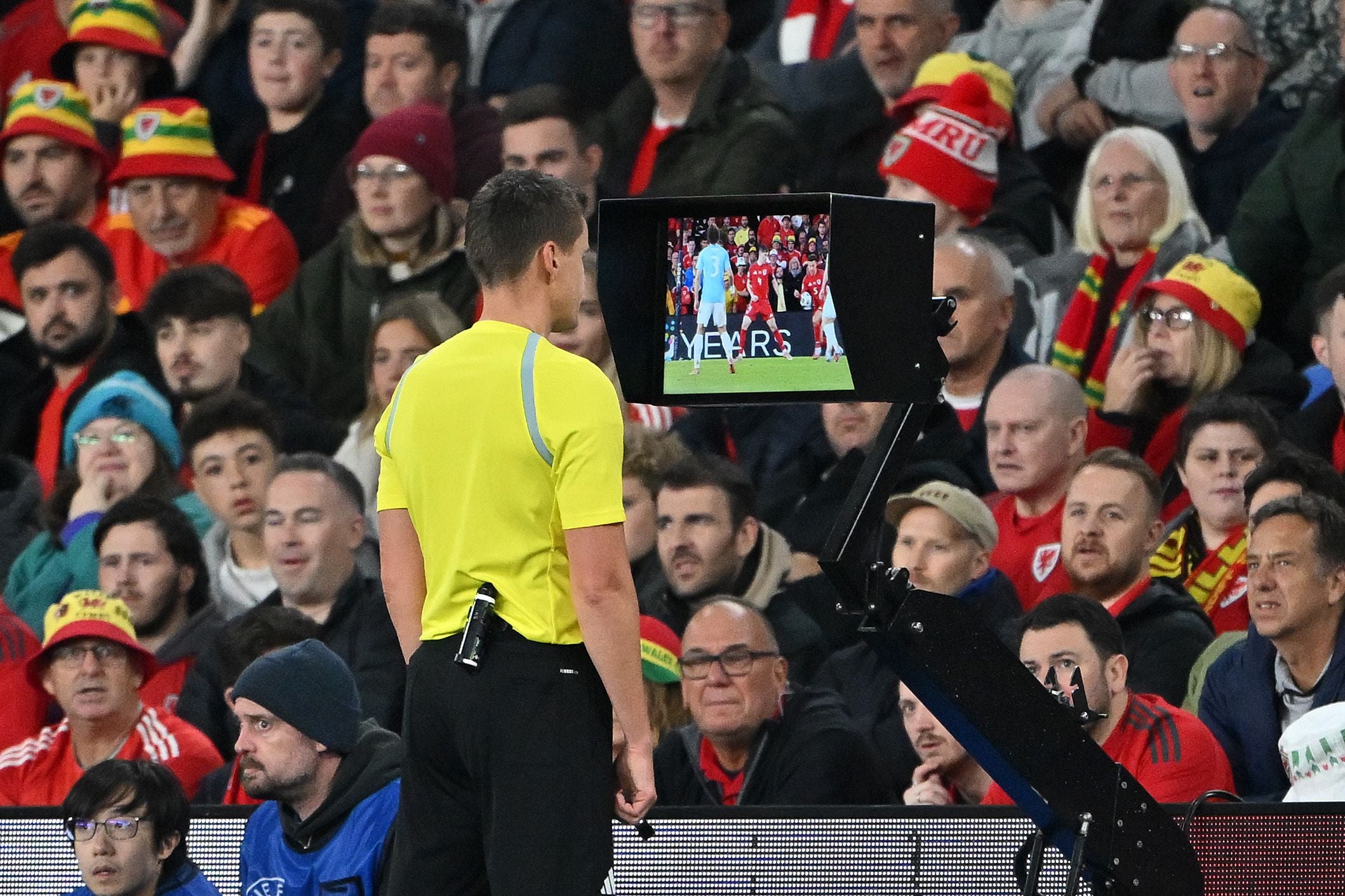 Ein Schiedsrichter betrachtet den VAR-Bildschirm vor einer Zuschauermenge im Fußballstadion.
