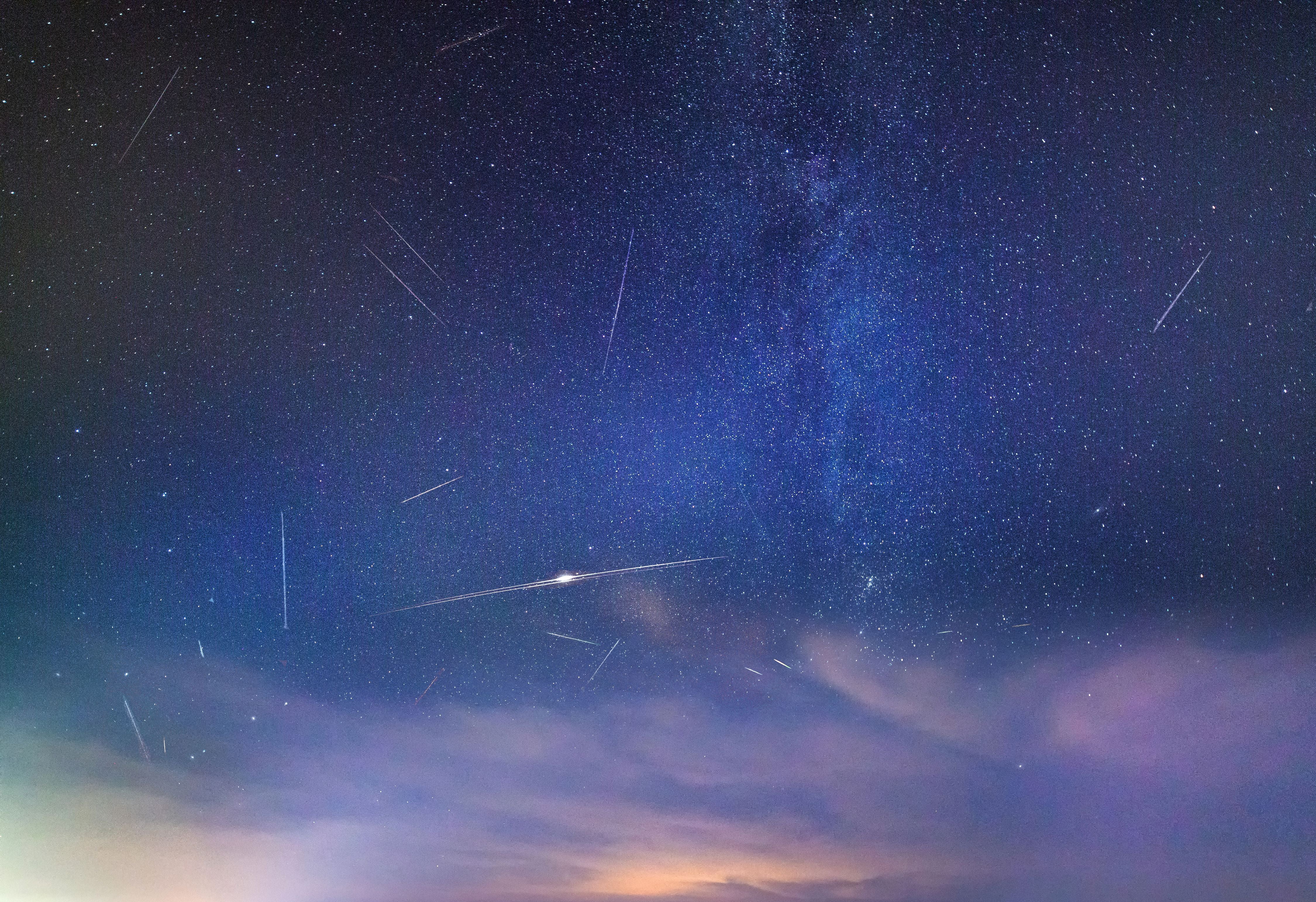 Viele Sternschnuppen am Nachthimmel während der Perseiden über einer Bucht mit leichten Wolken.