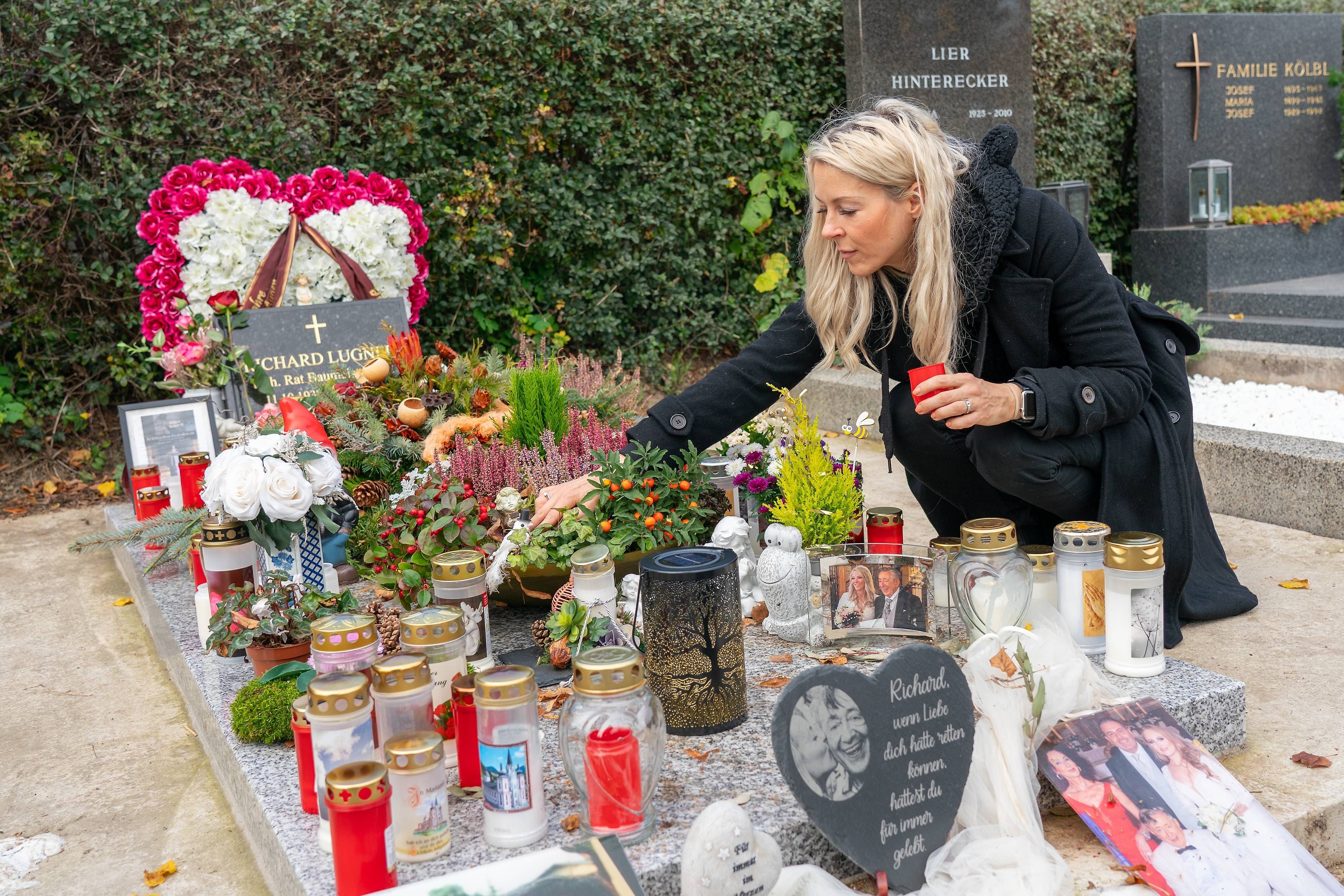 Eine Frau legt eine Kerze an einem bunt geschmückten Grab mit Fotos und Blumen nieder.
