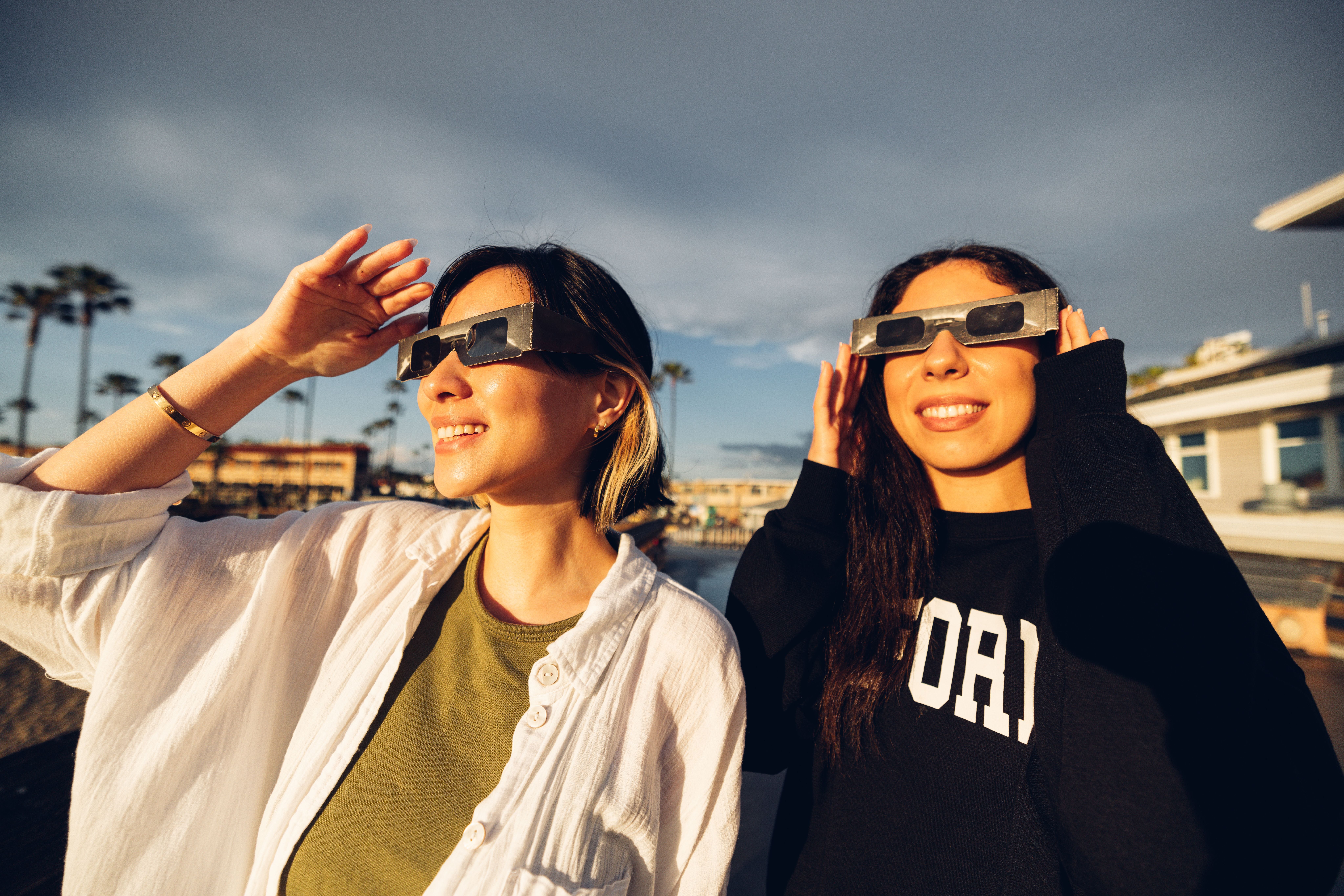 Zwei Frauen tragen Sonnenfinsternisbrillen und blicken lächelnd in die Sonne.