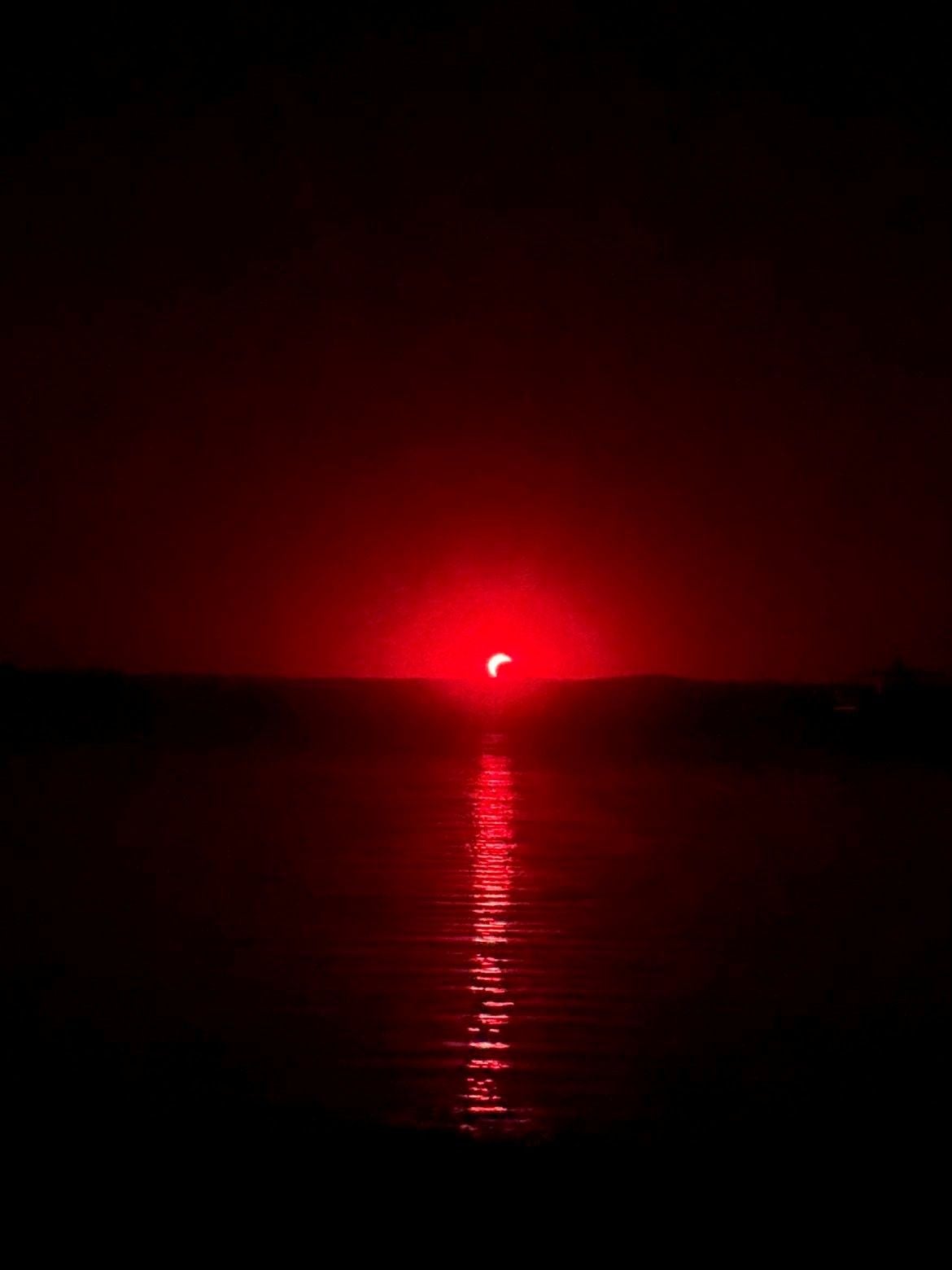 Rote Sonnenfinsternis über dem Neusiedler See bei Podersdorf, Spiegelung im Wasser sichtbar.