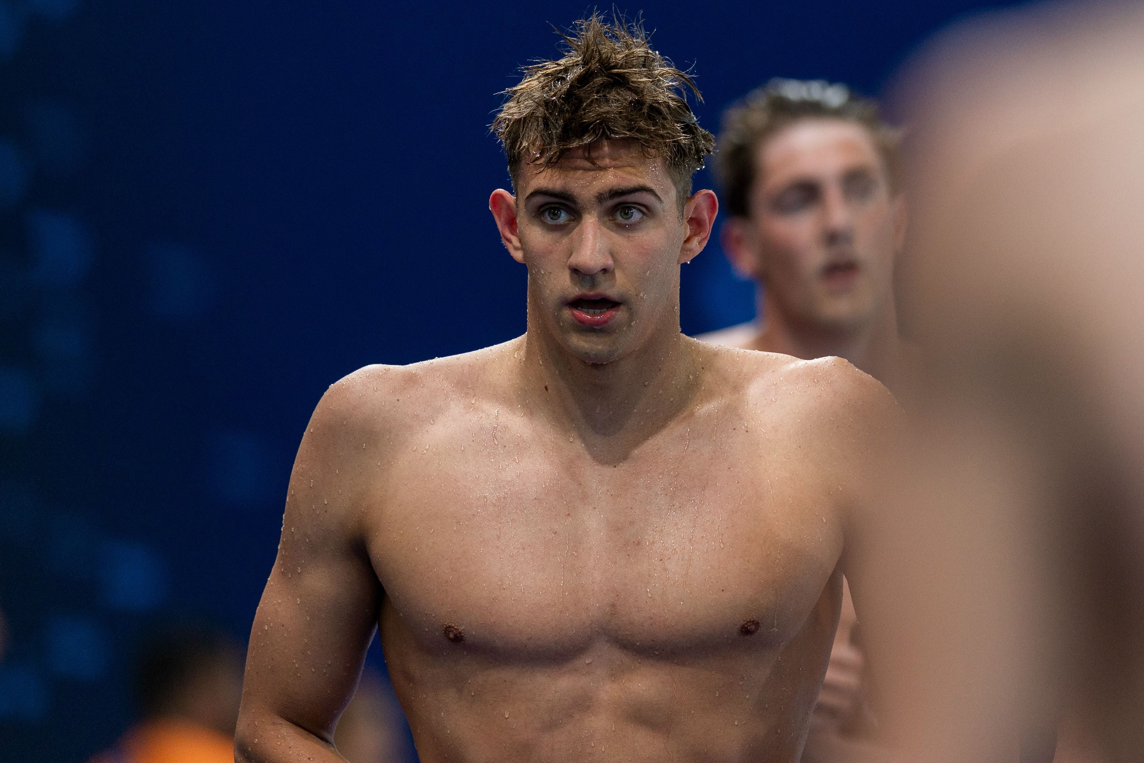 Ein nasser Schwimmer steht nach dem Wettkampf vor blauem Hintergrund.