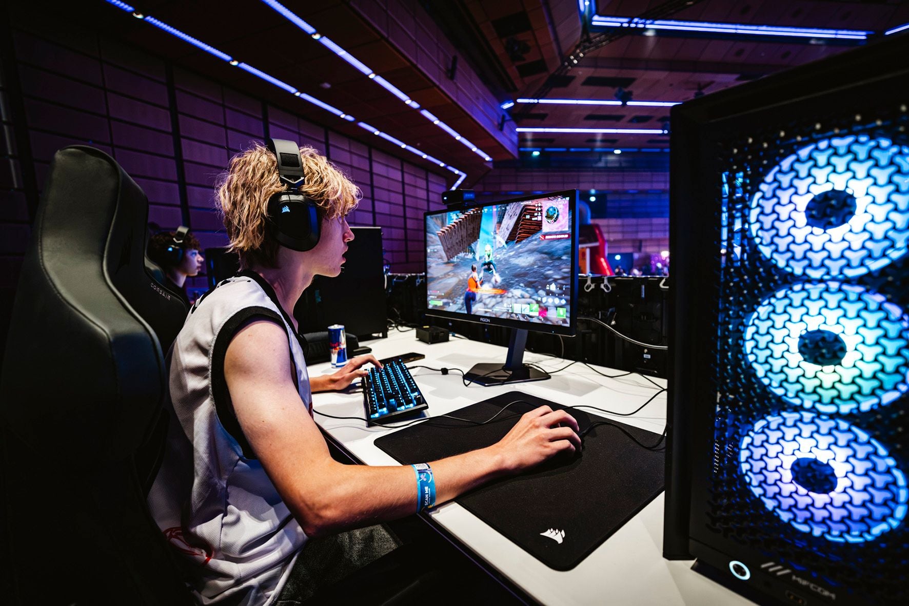 Junger Mann spielt konzentriert an einem Gaming-PC bei einem E-Sport-Turnier mit bunter Beleuchtung.