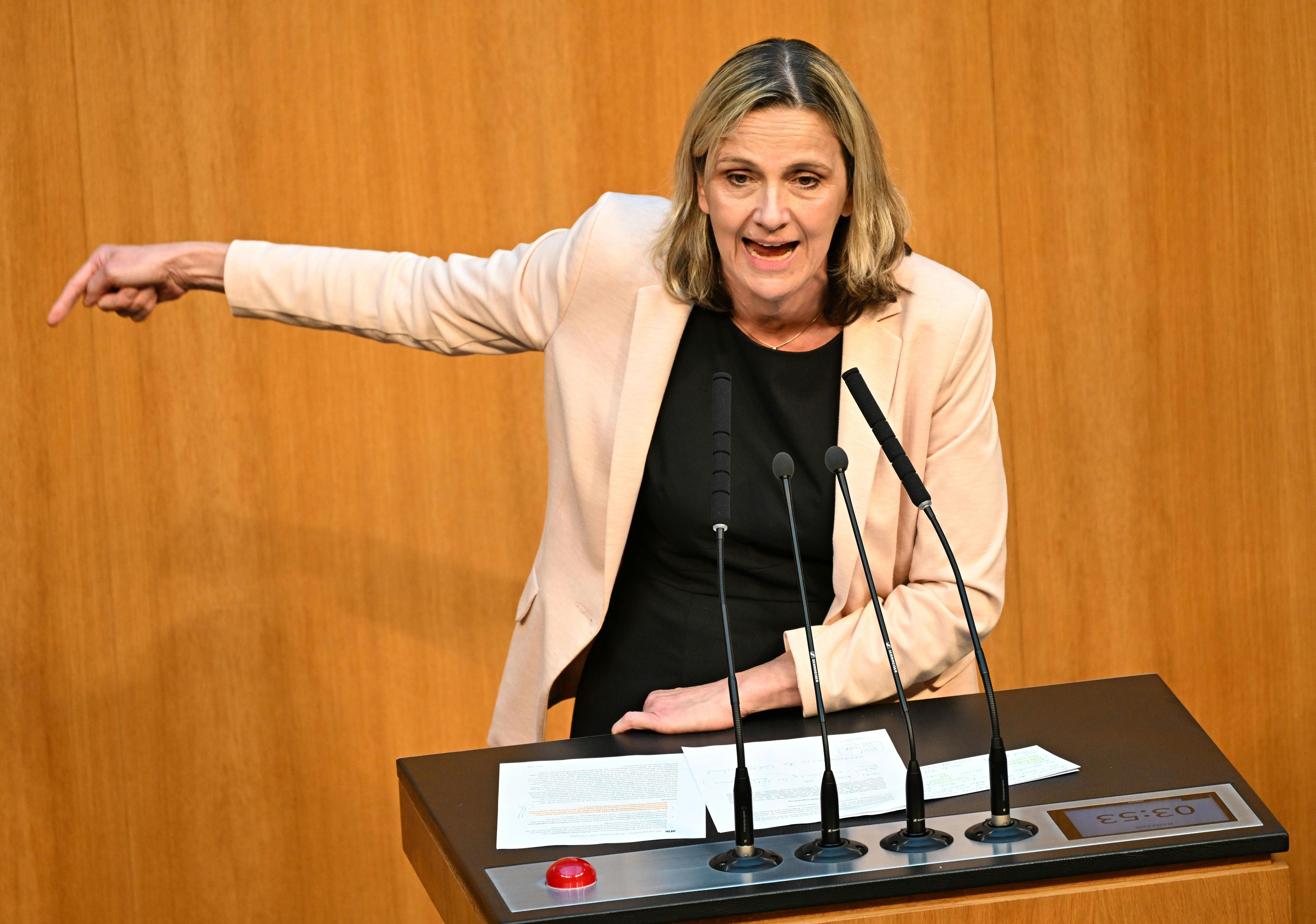 Eine Frau spricht gestikulierend am Rednerpult im Parlament vor Holzvertäfelung.