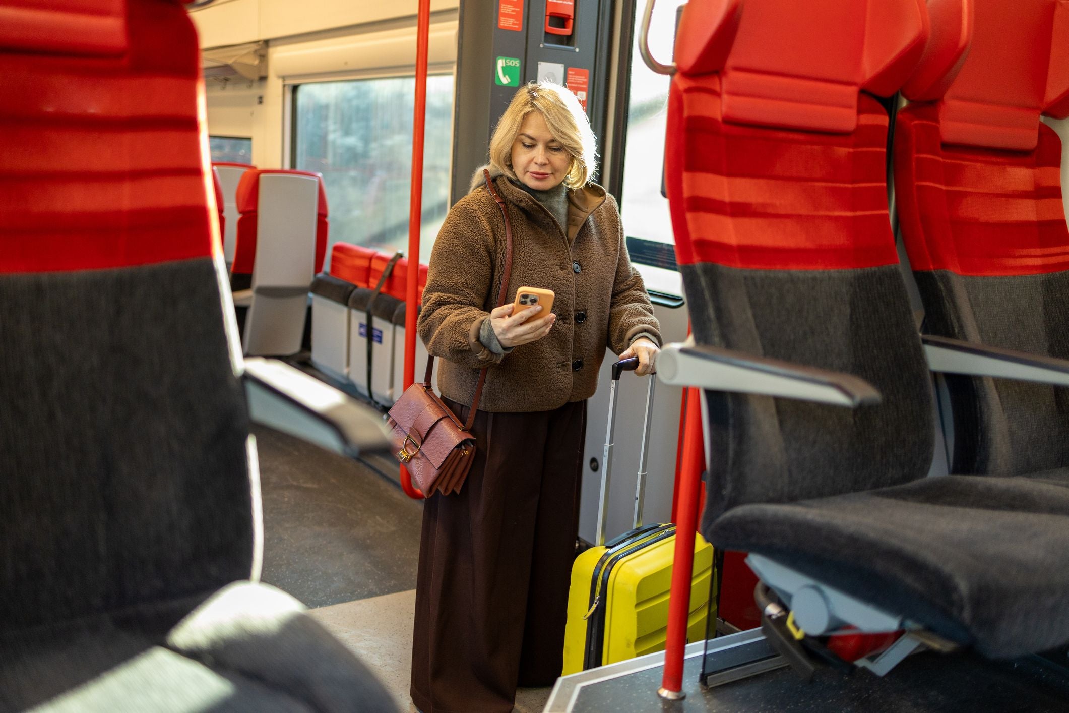 Frau mit gelbem Koffer schaut im Zug auf ihr Smartphone, moderne Sitze im Hintergrund.