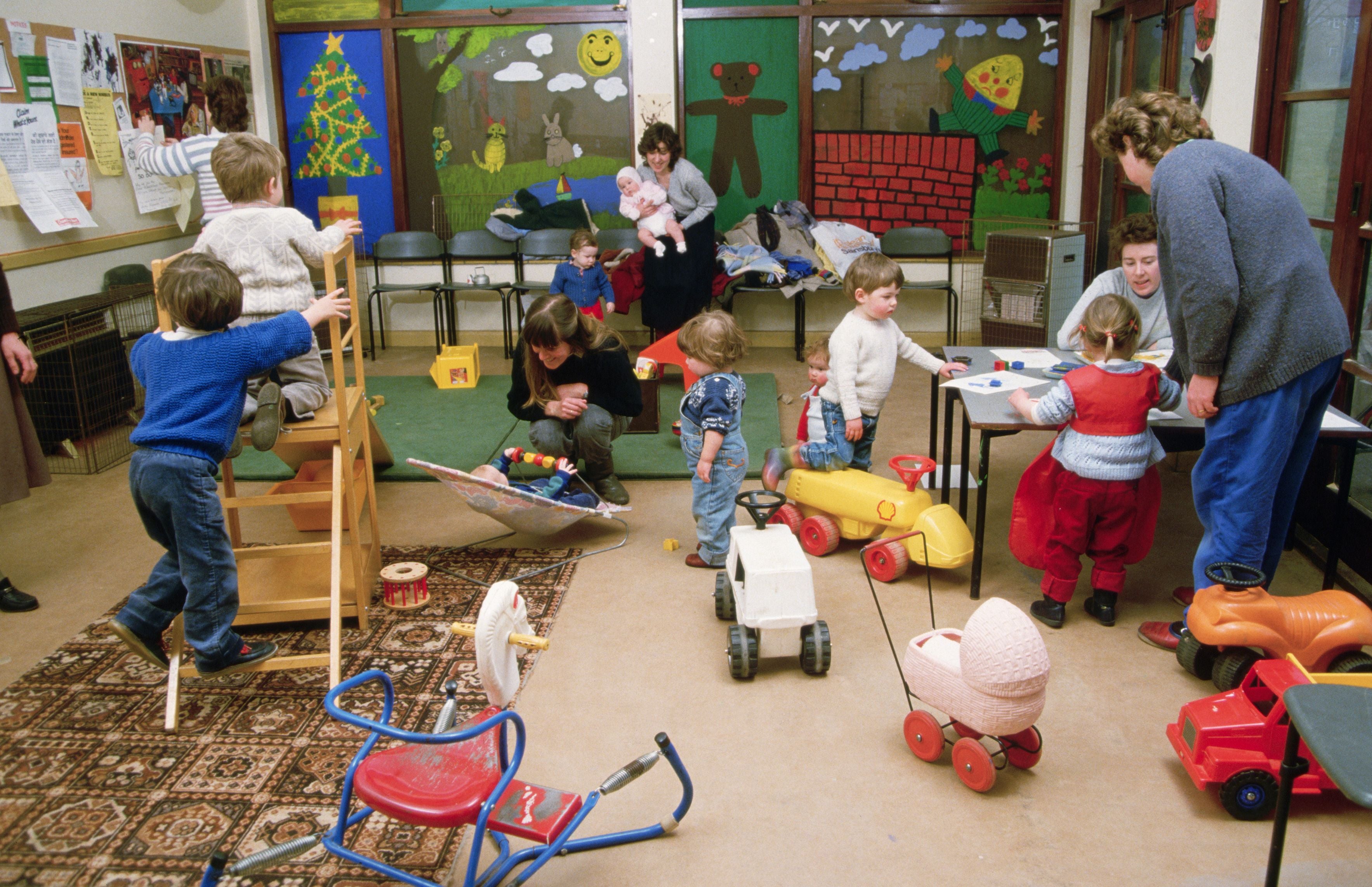 Kinder spielen in einem bunt dekorierten Kindergartenraum mit Spielzeug und werden von Erwachsenen betreut.