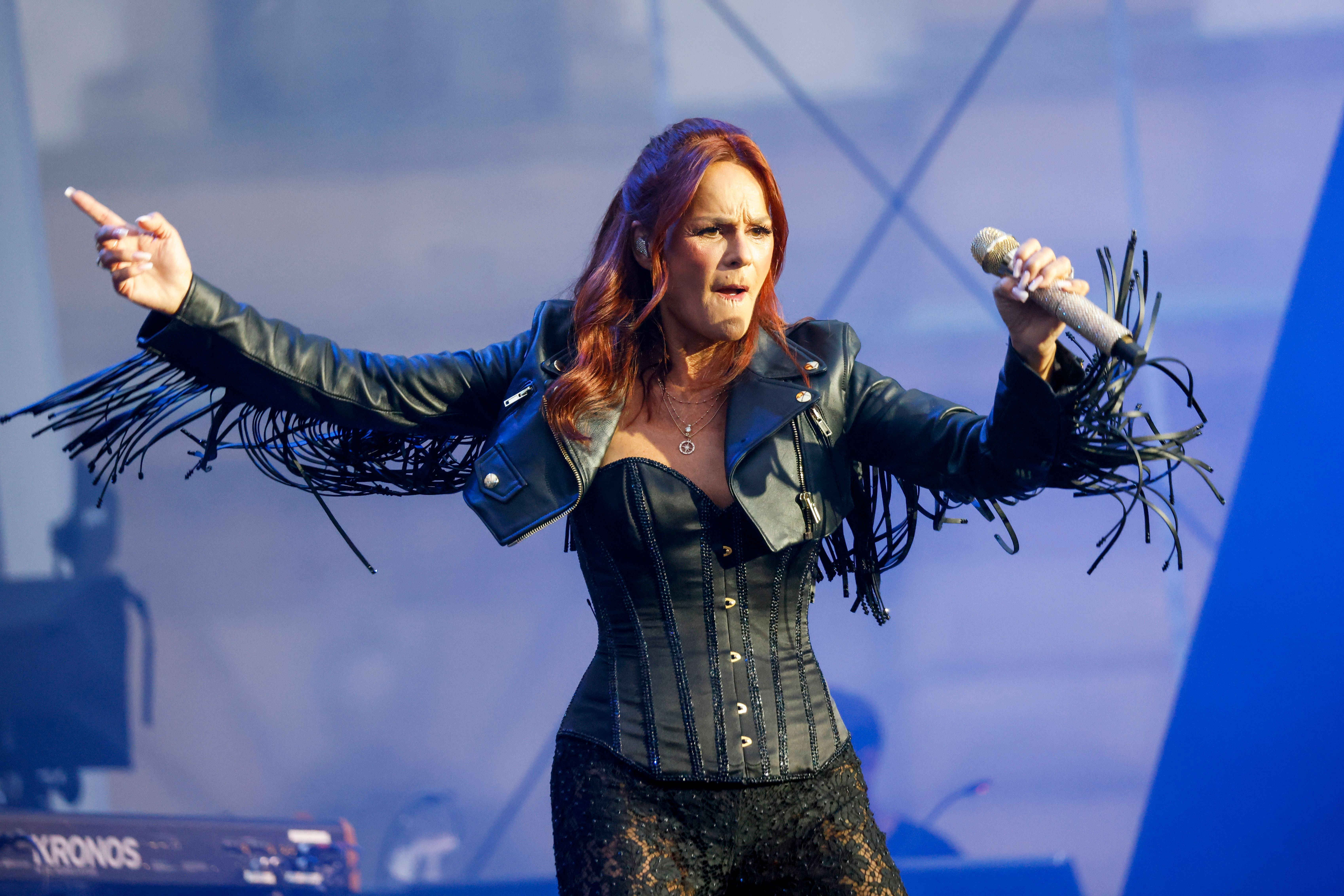 Andrea Berg singt auf einer Bühne mit Mikrofon, Lederjacke und schwarzem Korsett.