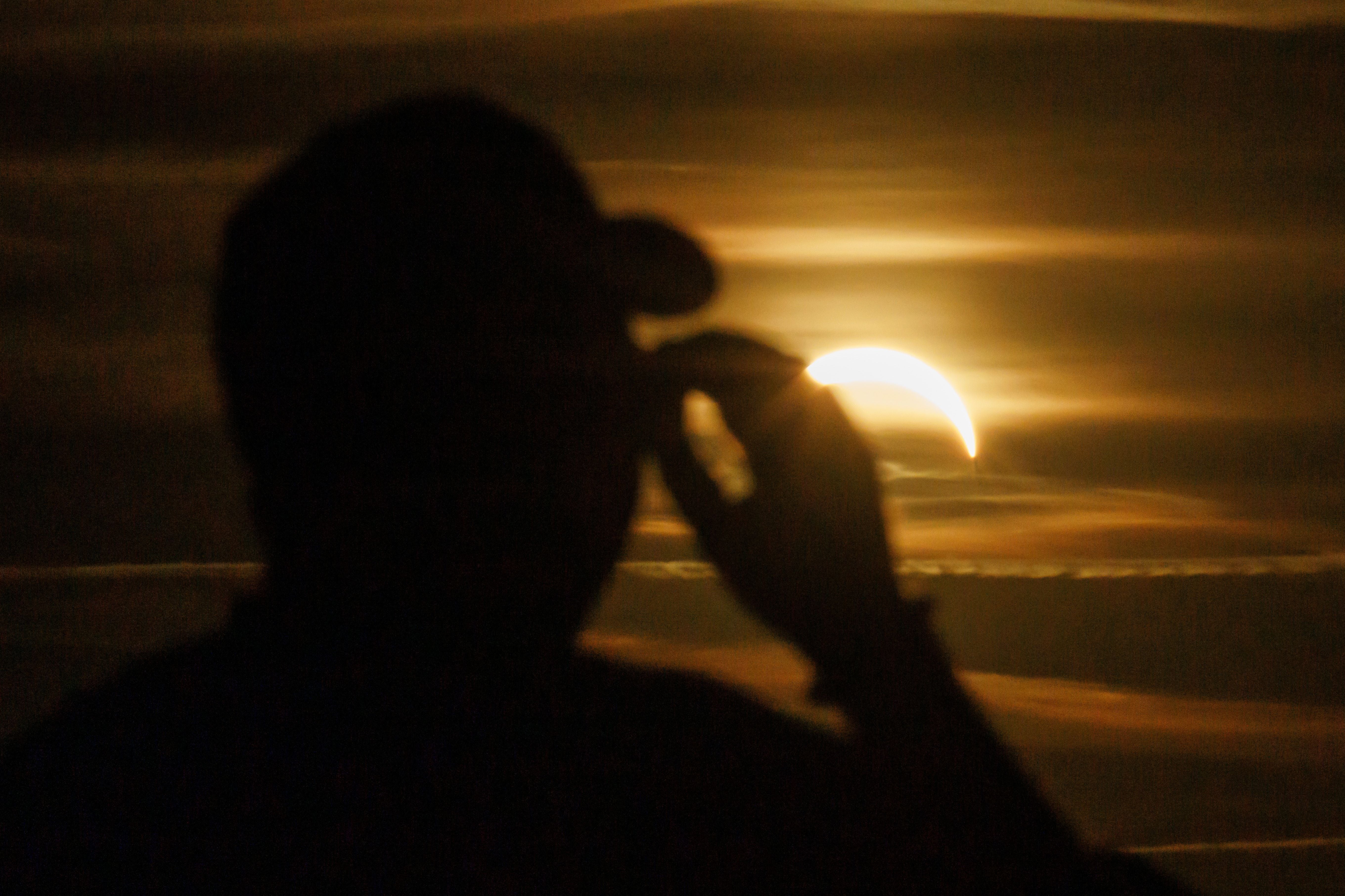 Schattenriss einer Person mit Schutzbrille vor teilweiser Sonnenfinsternis am Abendhimmel.