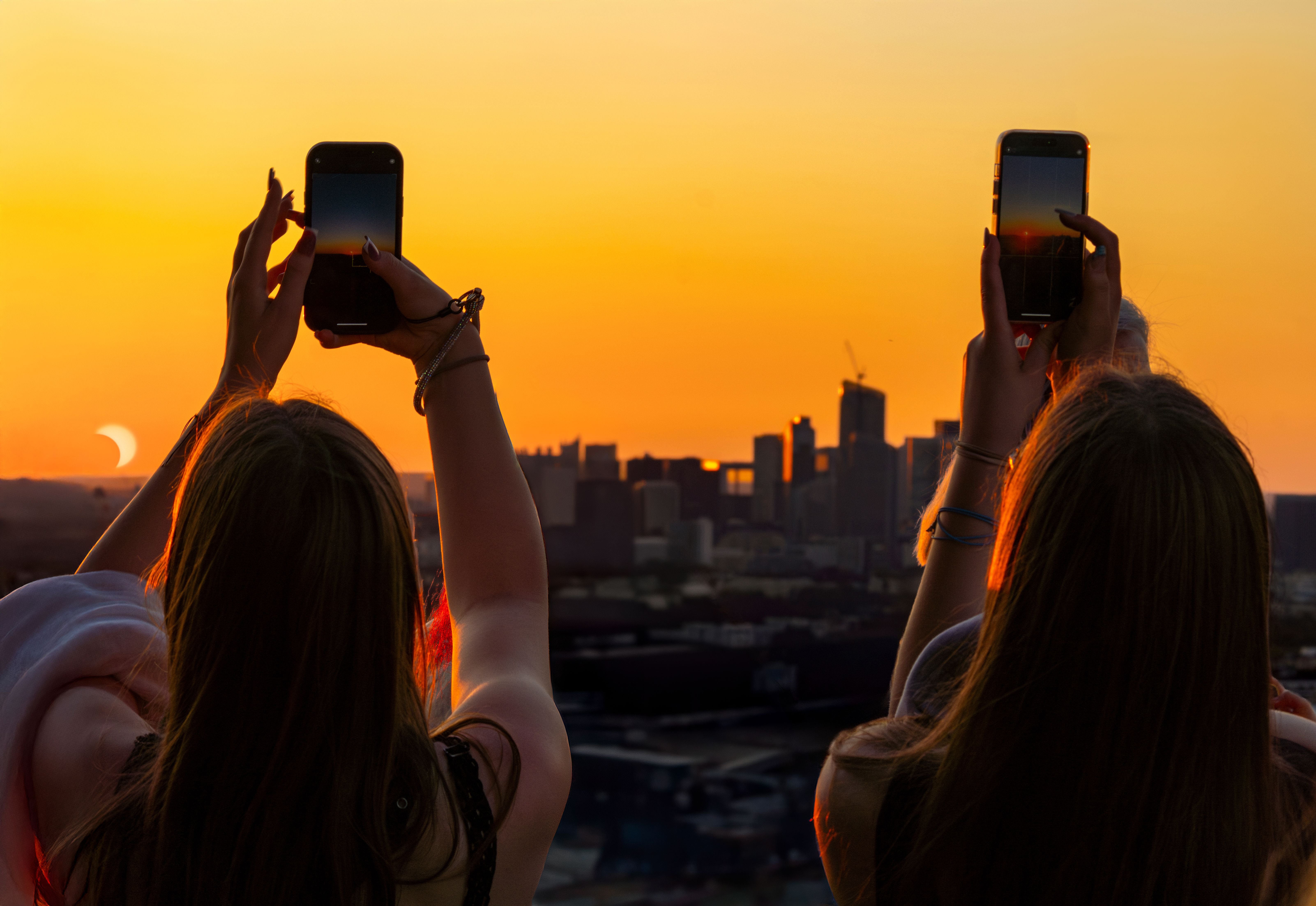 Zwei Personen fotografieren eine partielle Sonnenfinsternis über Paris bei Sonnenuntergang.