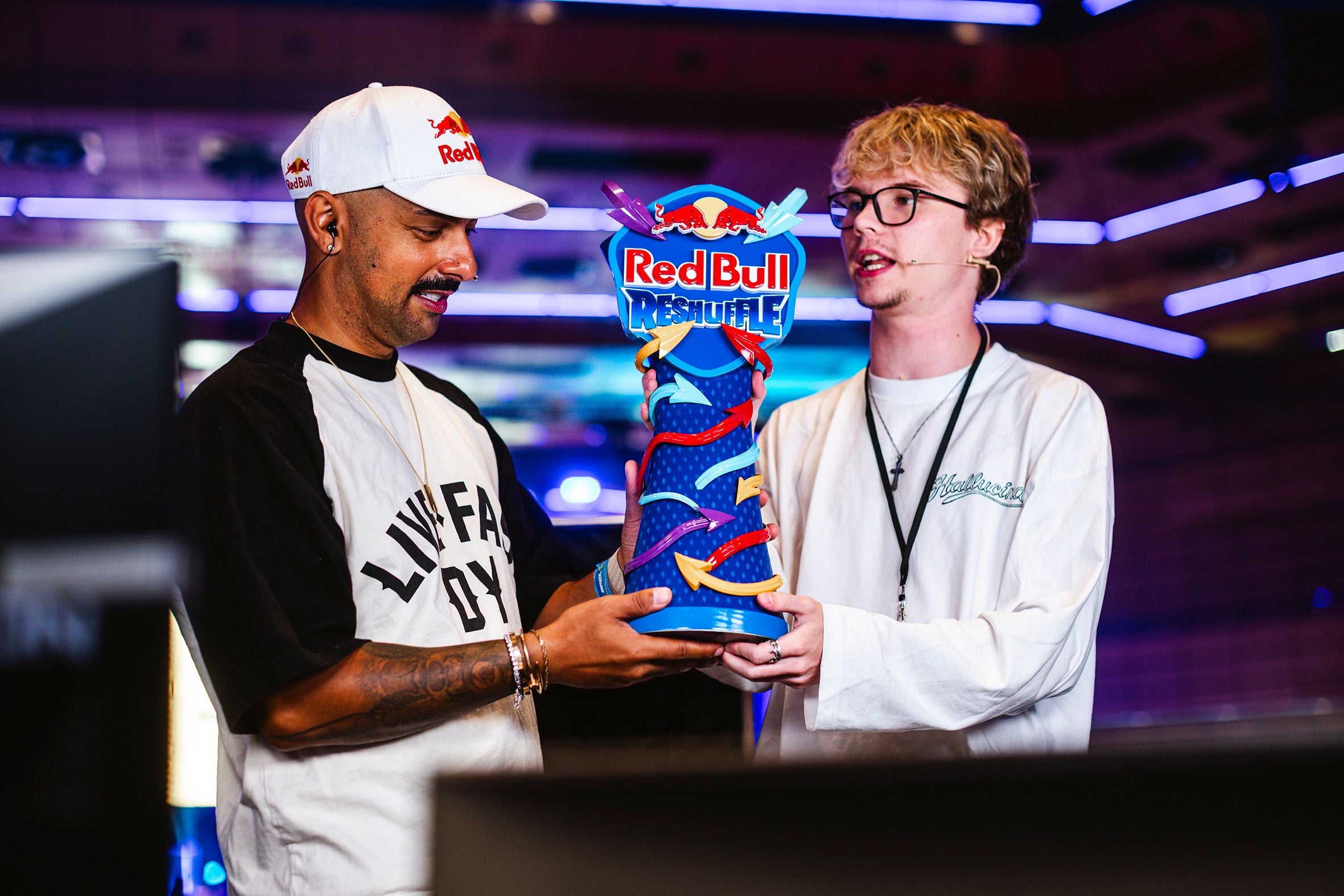 Zwei Männer präsentieren die bunte Red Bull Reshuffle Trophäe bei einem eSports-Event.