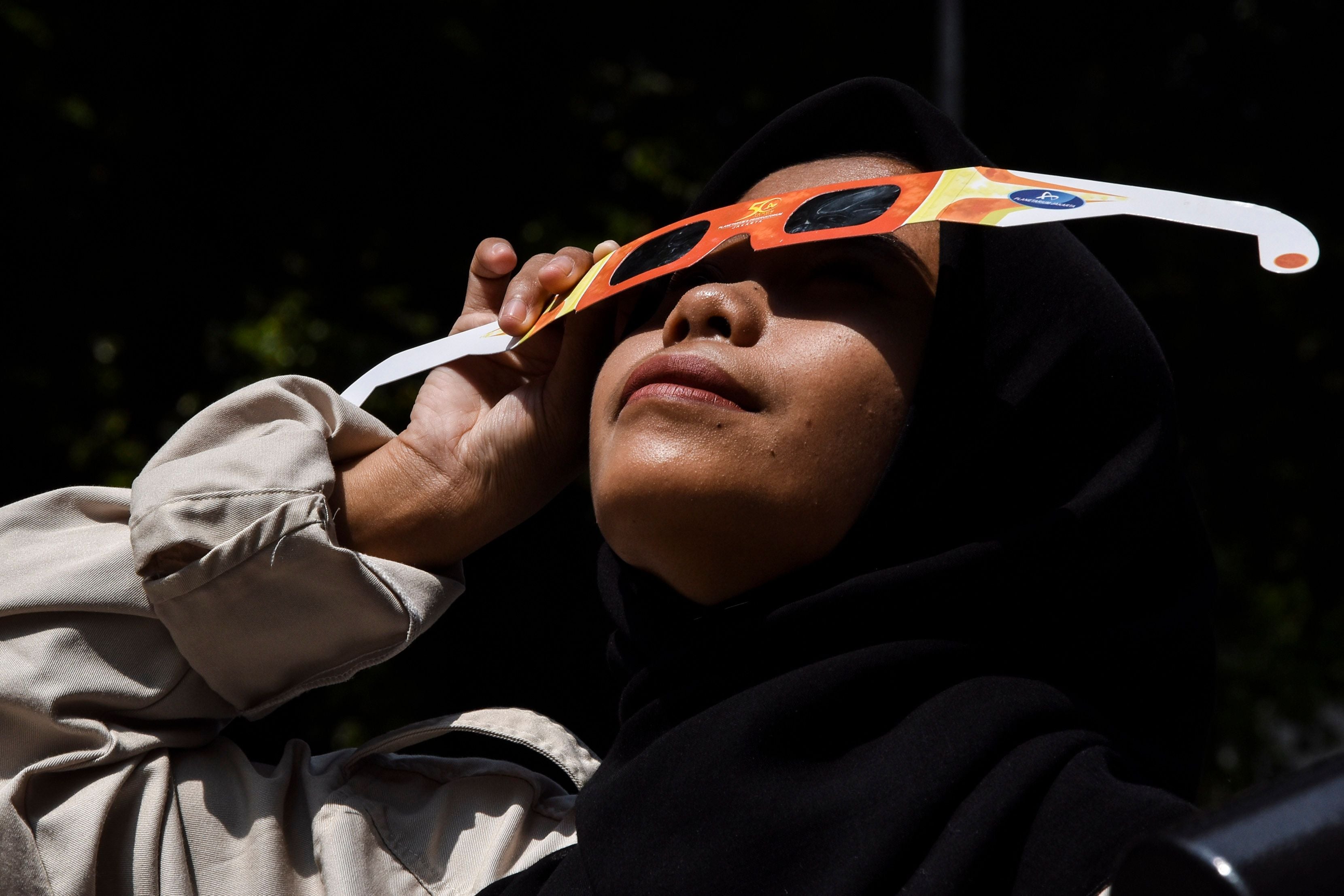 Frau mit Sonnenfinsternisbrille blickt bei Sonnenfinsternis in den Himmel.