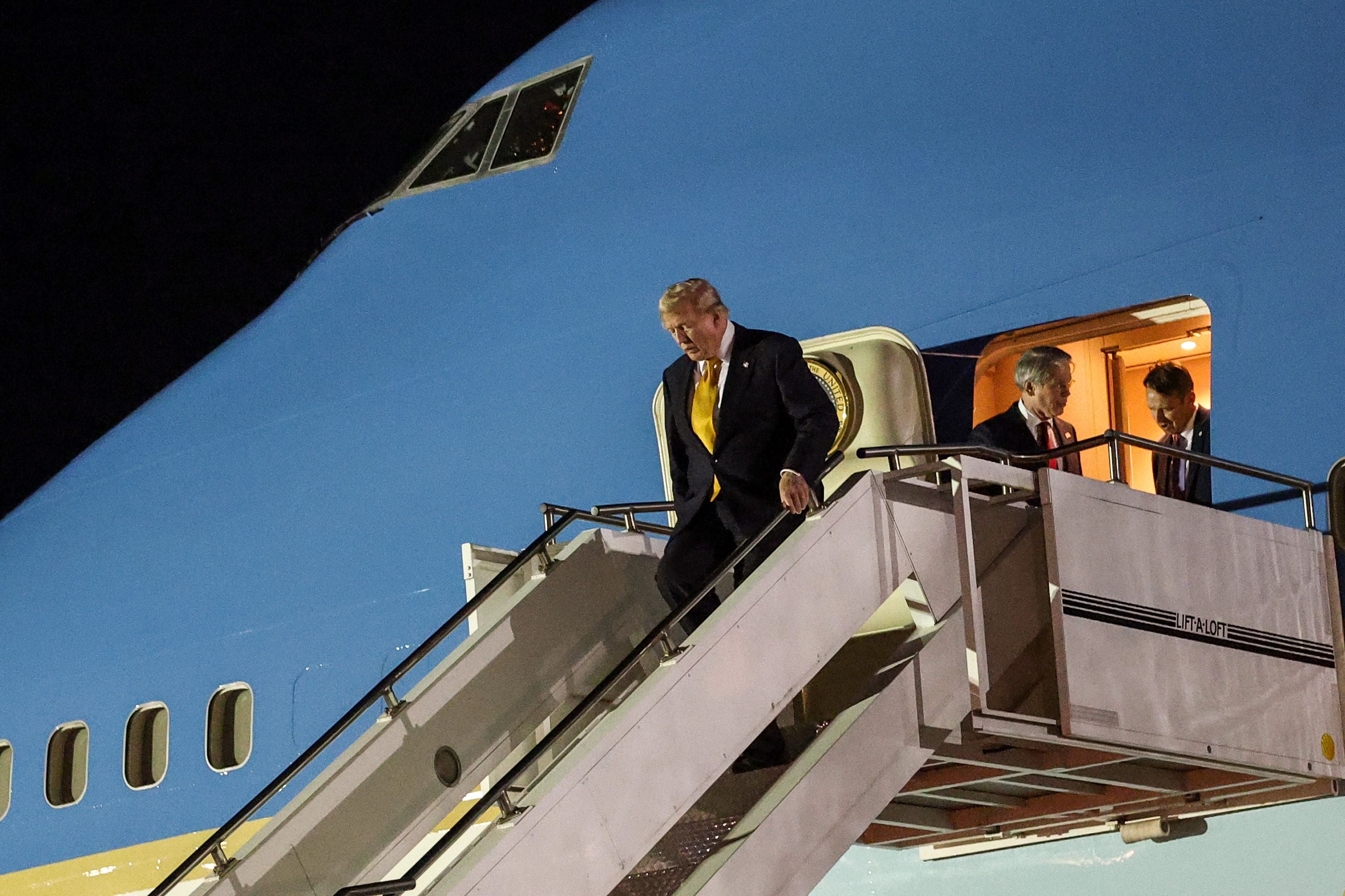 Ein Mann im Anzug steigt abends eine Flugzeugtreppe an einem großen blauen Flugzeug hinab.