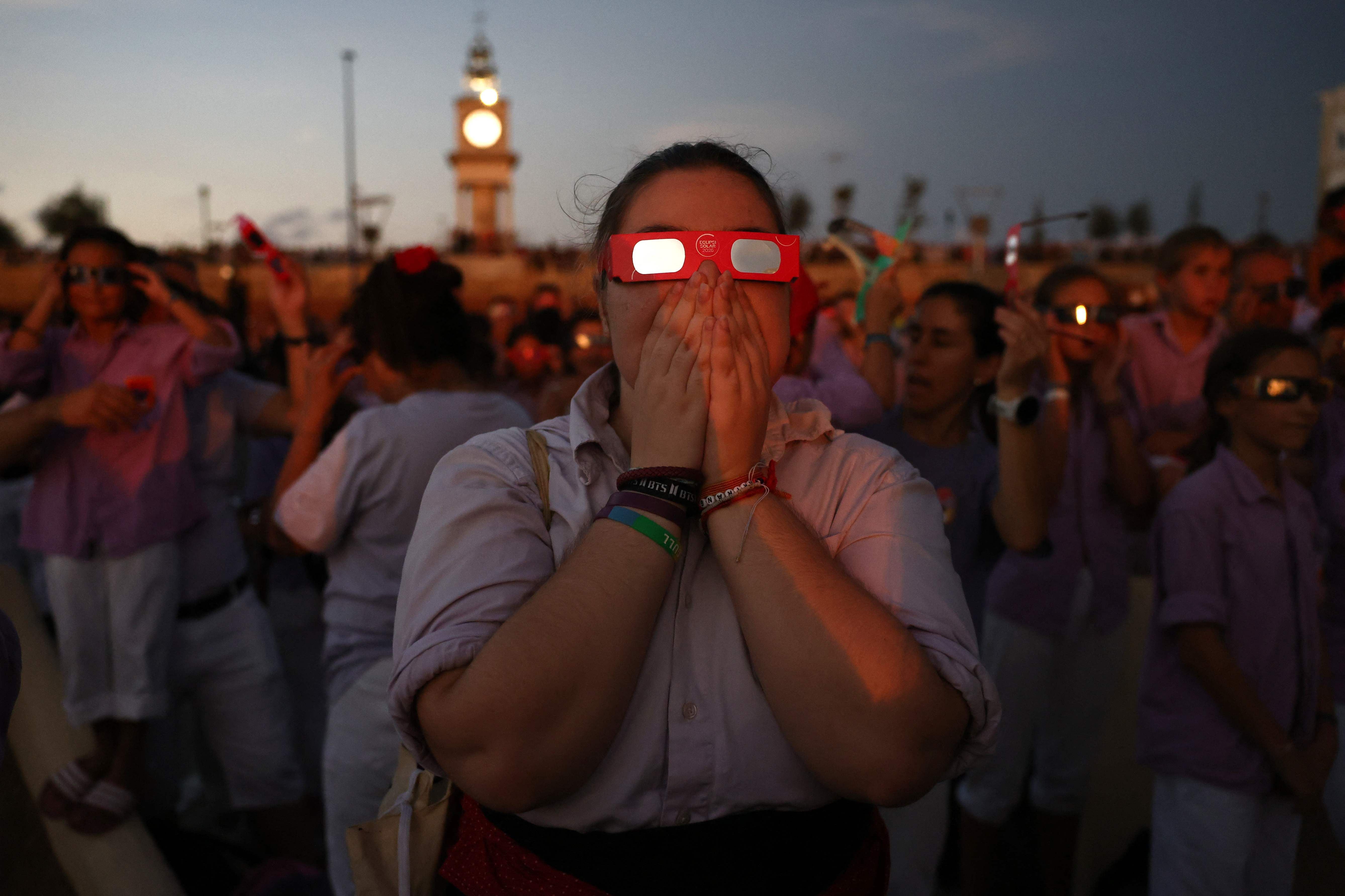Menschen mit Schutzbrillen beobachten eine Sonnenfinsternis am Hafen von Tarragona, Spanien, bei Dämmerung.
