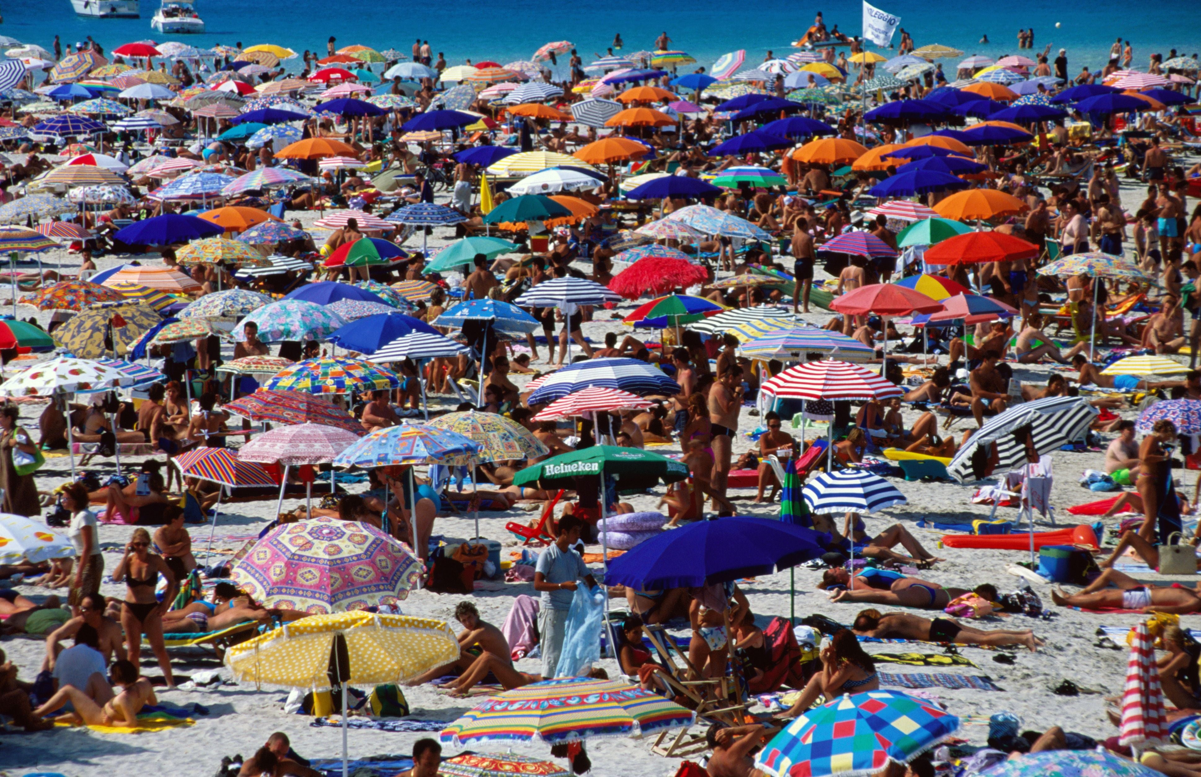 Überfüllter Strand mit vielen bunten Sonnenschirmen und Menschen in Stintino, Sardinien.