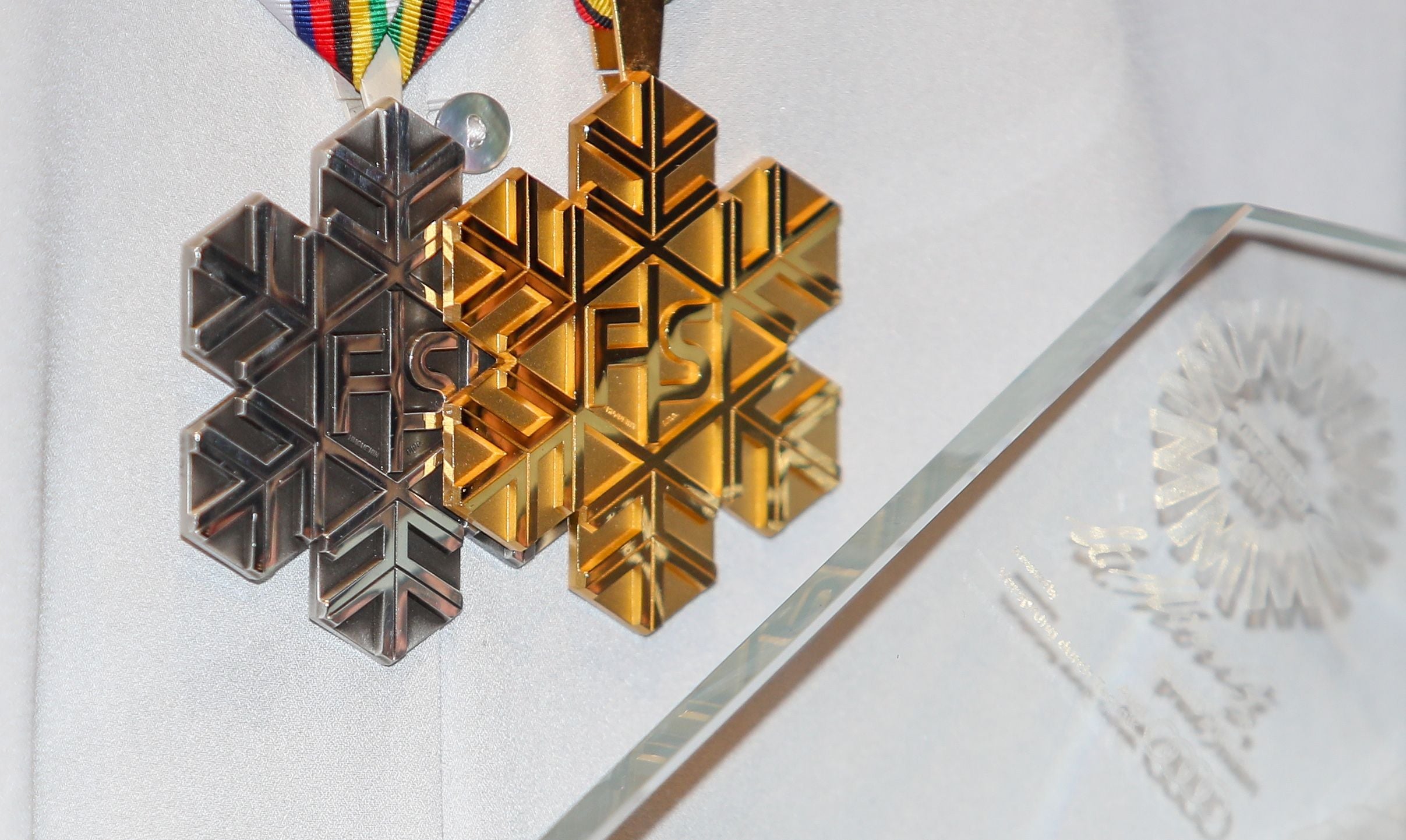 Eine silberne und eine goldene Schneeflocken-Medaille hängen nebeneinander an Bändern.