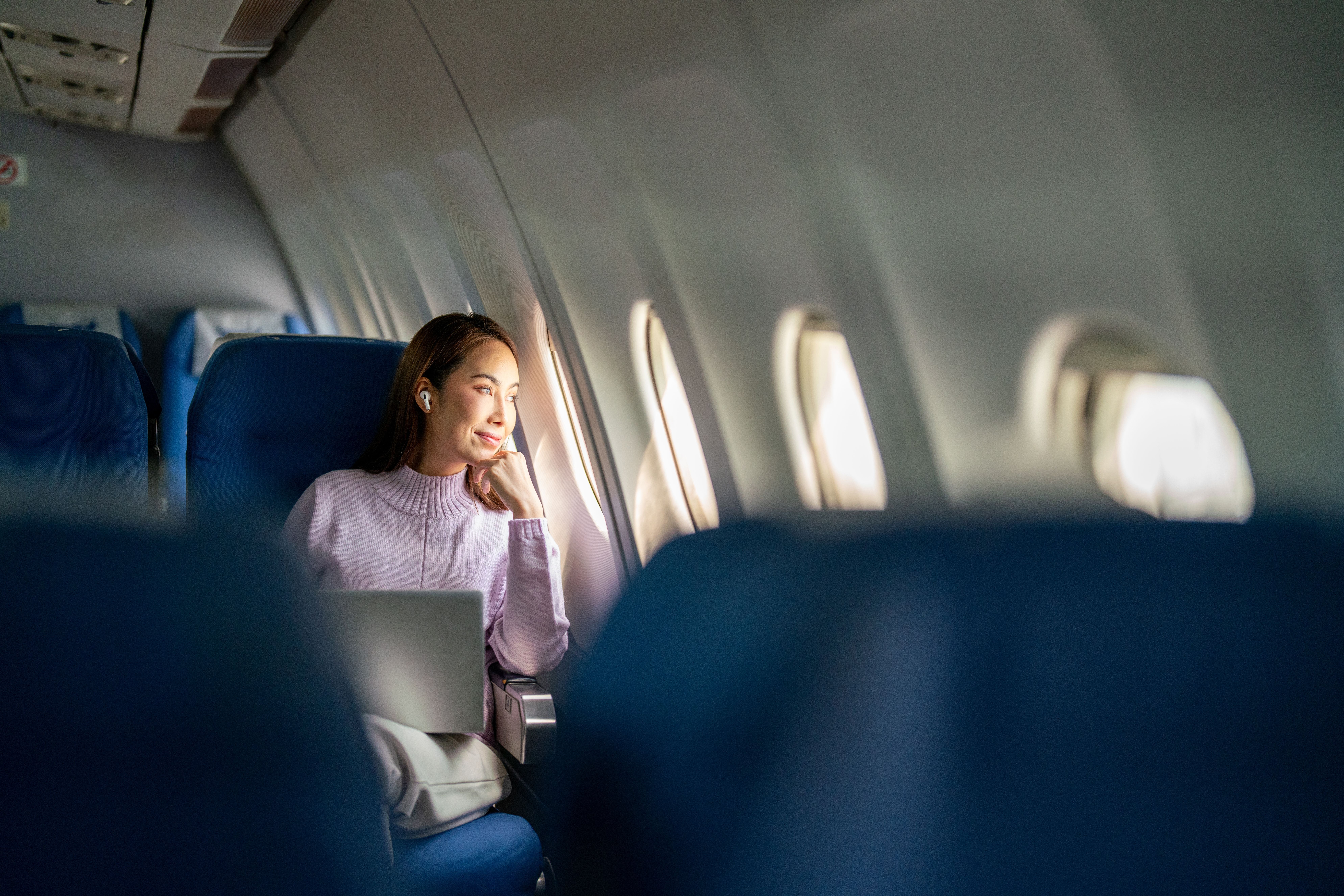 Frau mit Laptop blickt entspannt aus dem Fenster eines Flugzeugs.