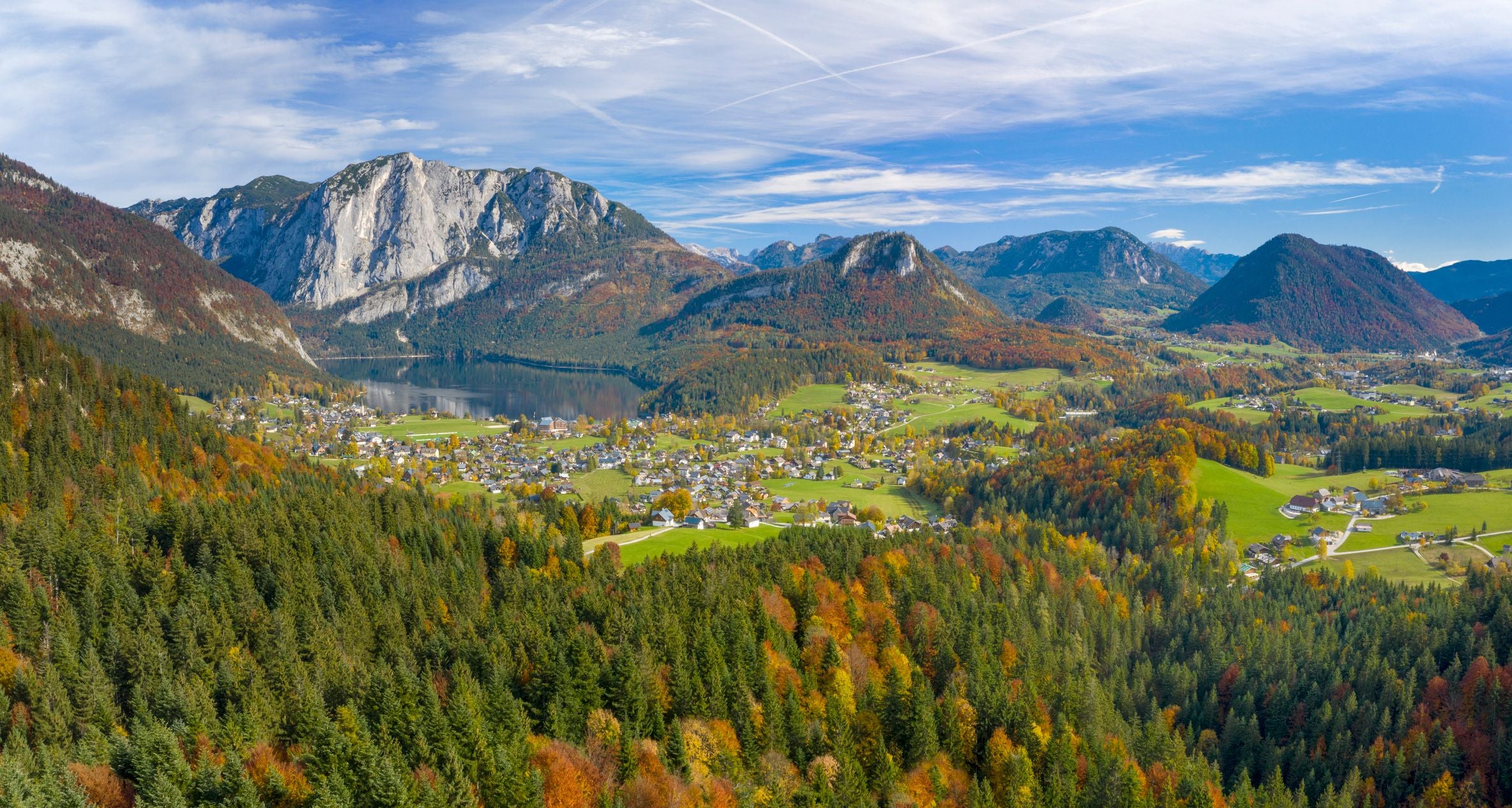 Herbstliche Panoramaaufnahme vom Altausseer See mit Alpen, Wäldern und Dörfern im Vordergrund.