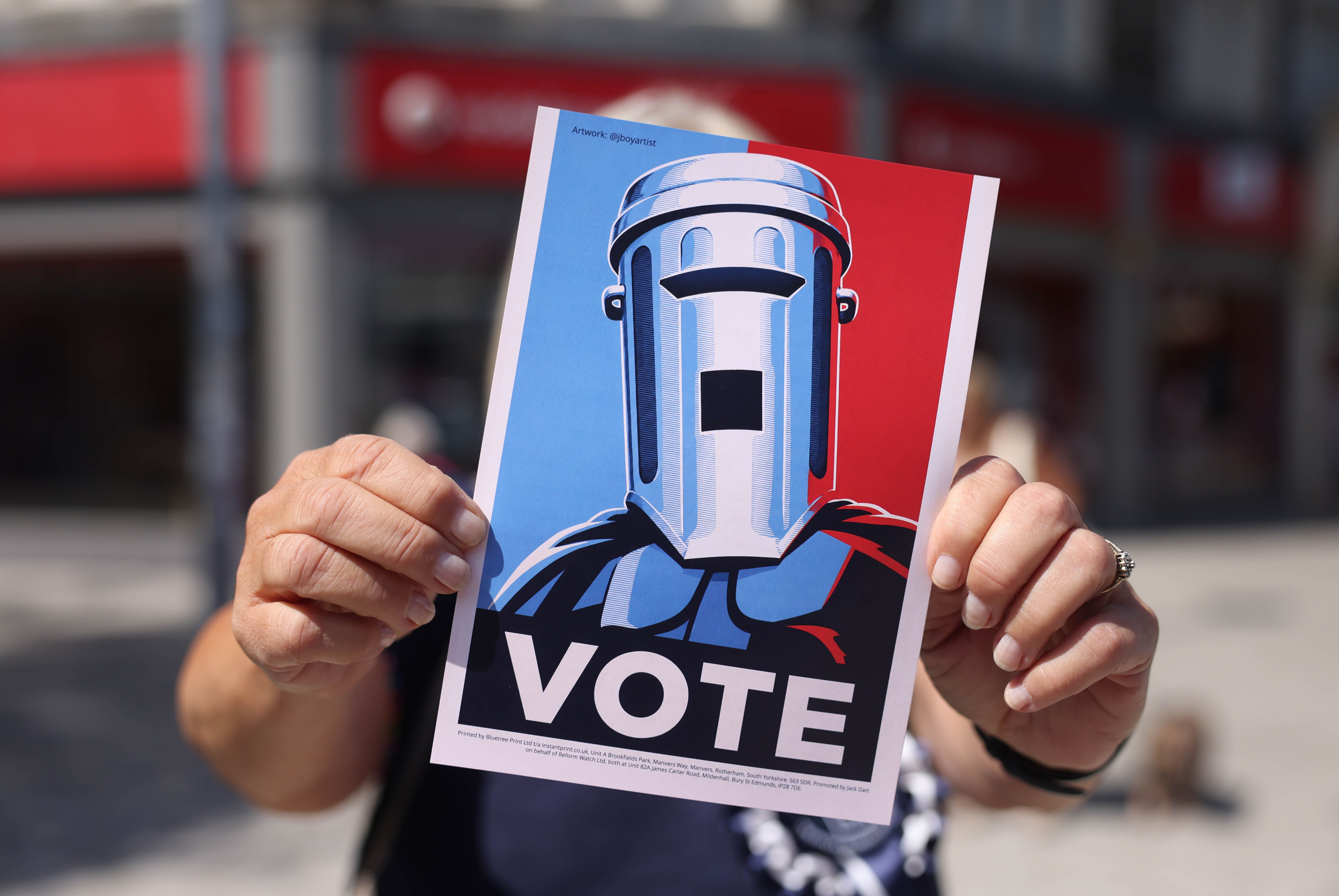 Eine Person hält ein Plakat mit Count Binface und dem Schriftzug „VOTE“ in die Kamera.