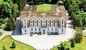 Großes, rechteckiges Gebäude mit begrüntem Dach, umgeben von Bäumen, aus der Vogelperspektive.