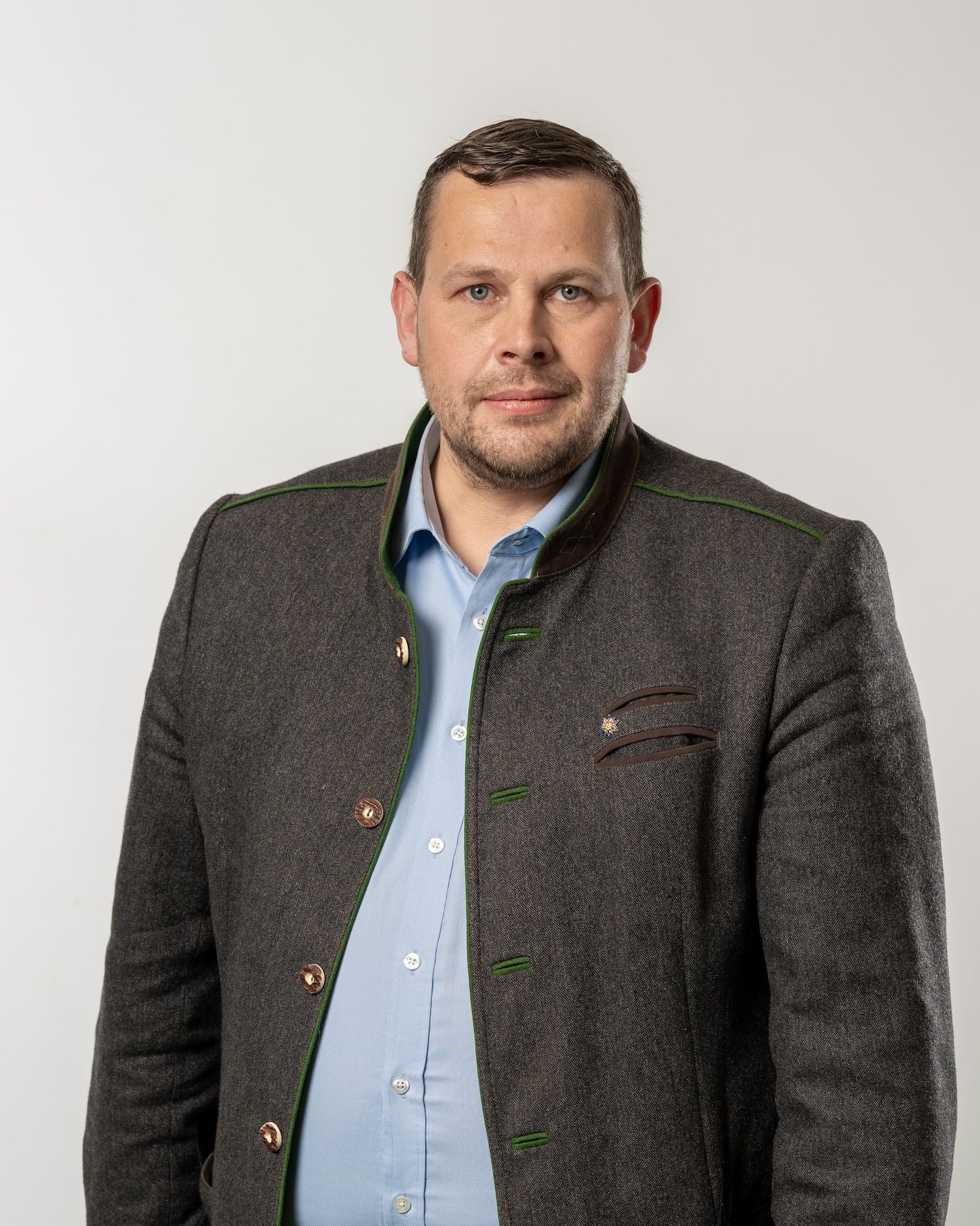 Mann in Trachtenjacke und hellblauem Hemd vor neutralem Hintergrund.