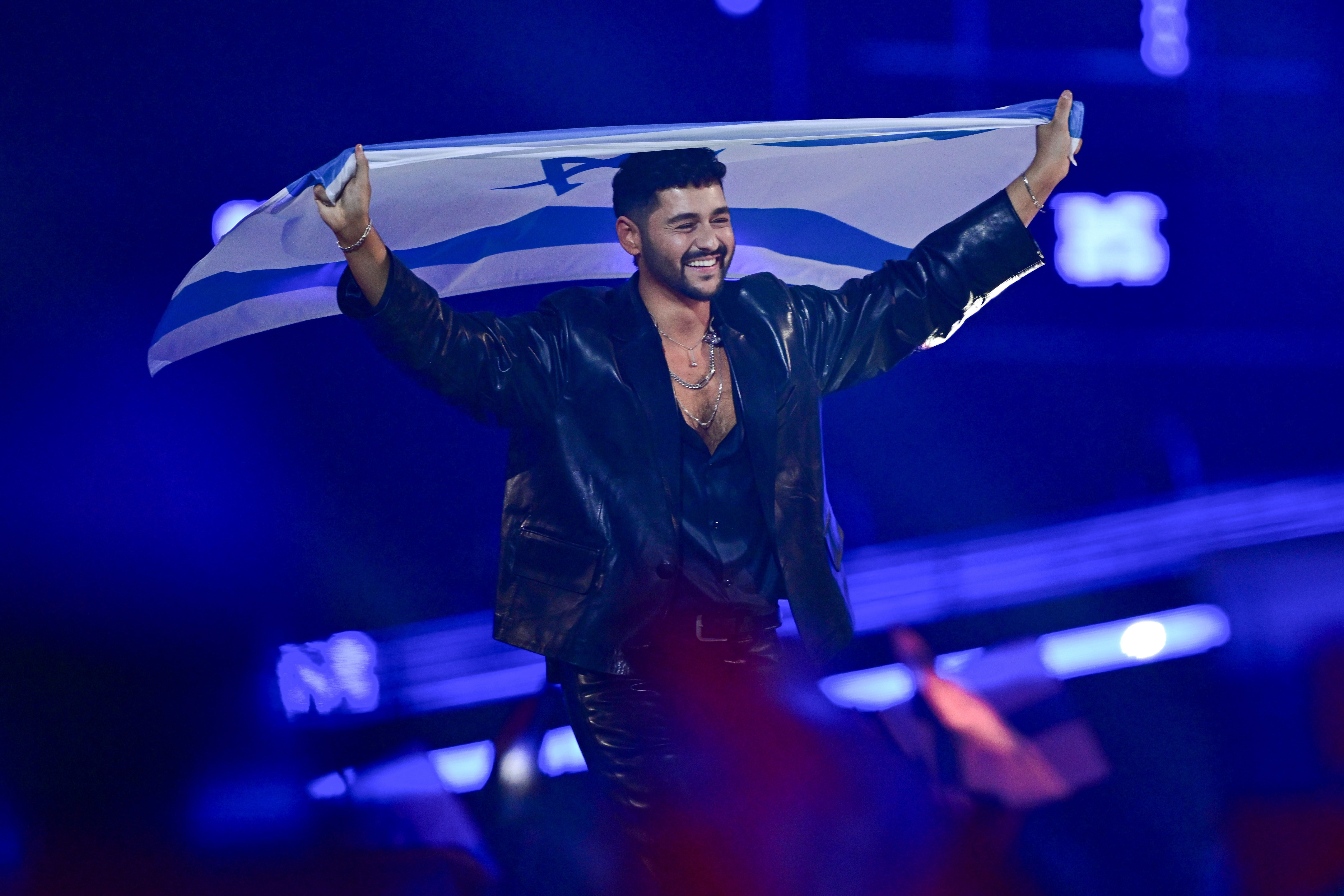 Ein Mann im schwarzen Anzug trägt eine israelische Flagge auf einer Bühne mit blauem Licht.