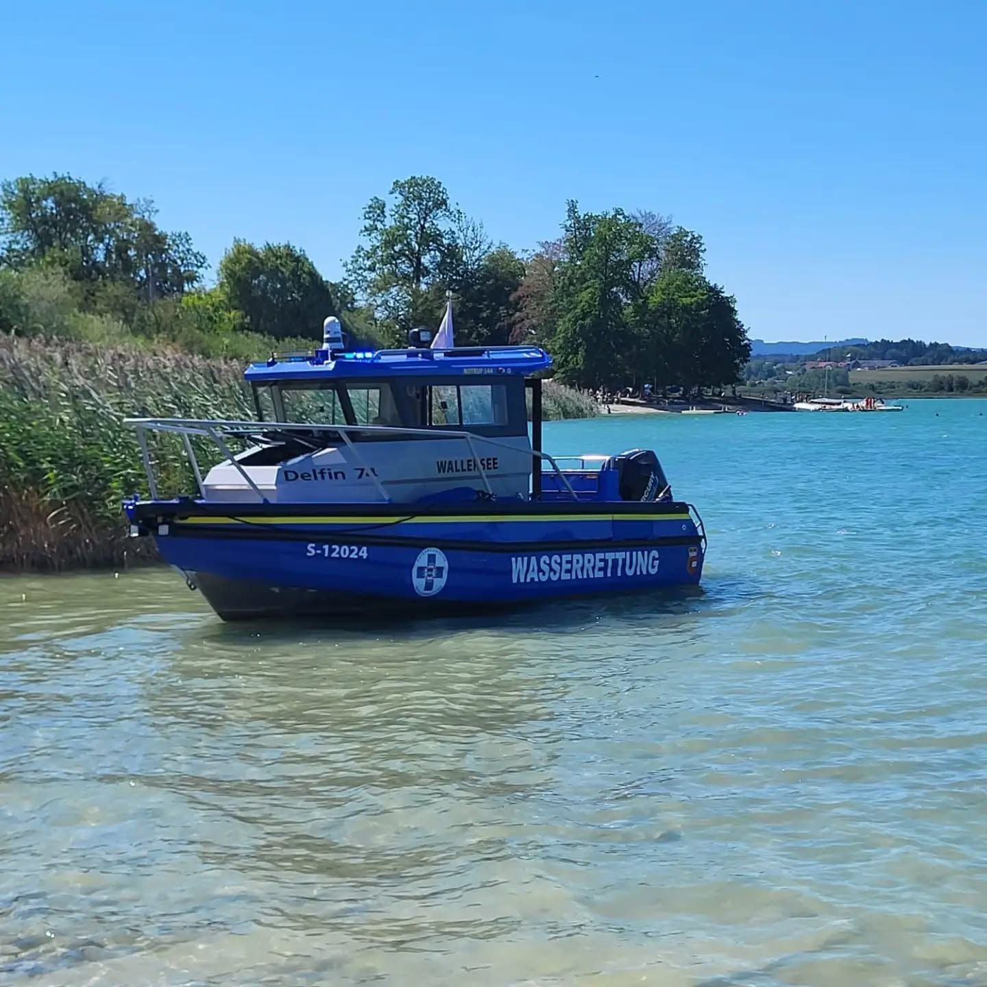 Ein blaues Wasserrettungsboot liegt im flachen Wasser am Ufer eines Sees.