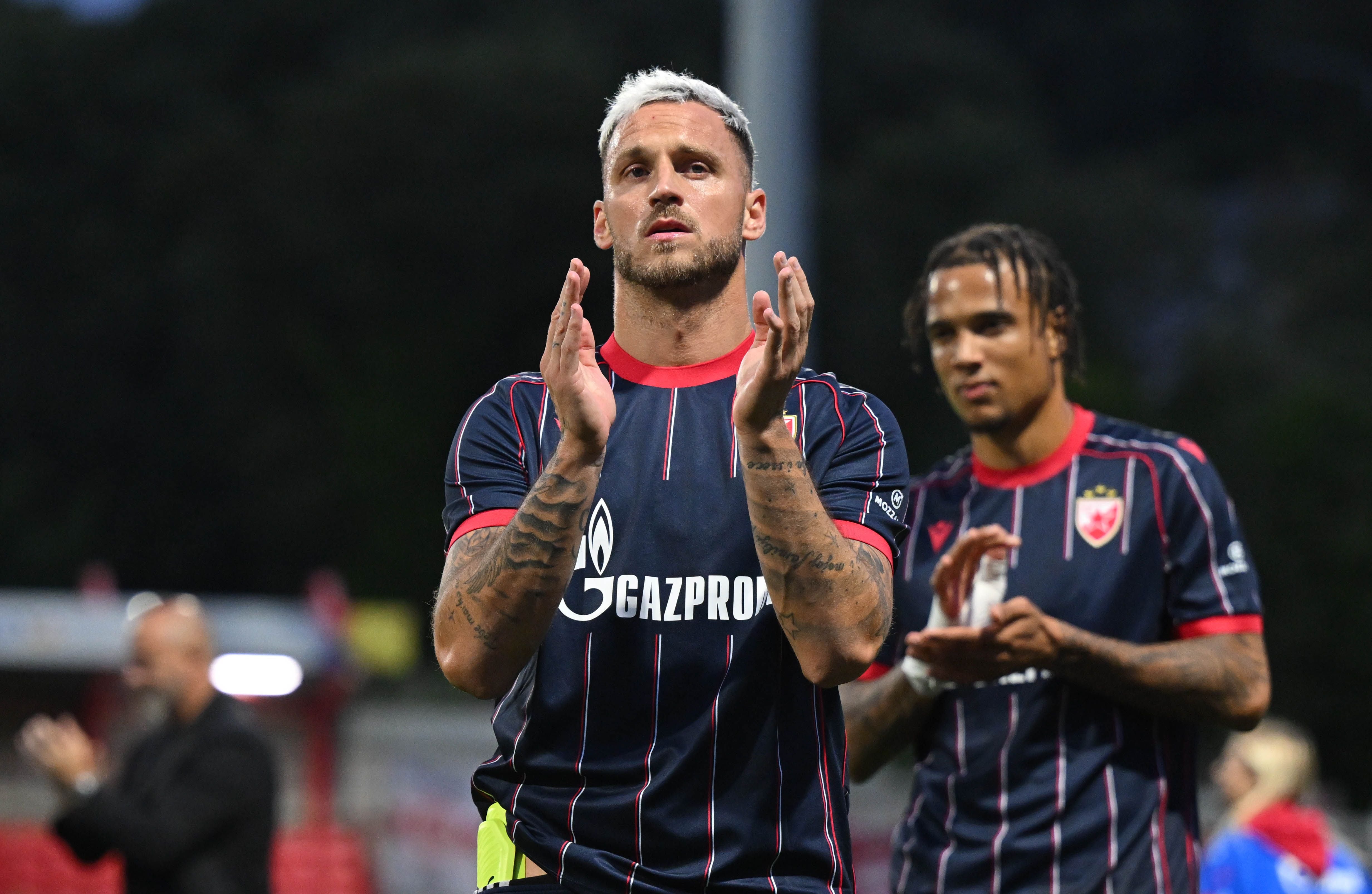 Zwei Fußballspieler von Roter Stern Belgrad applaudieren nach einem Spiel auf dem Spielfeld.