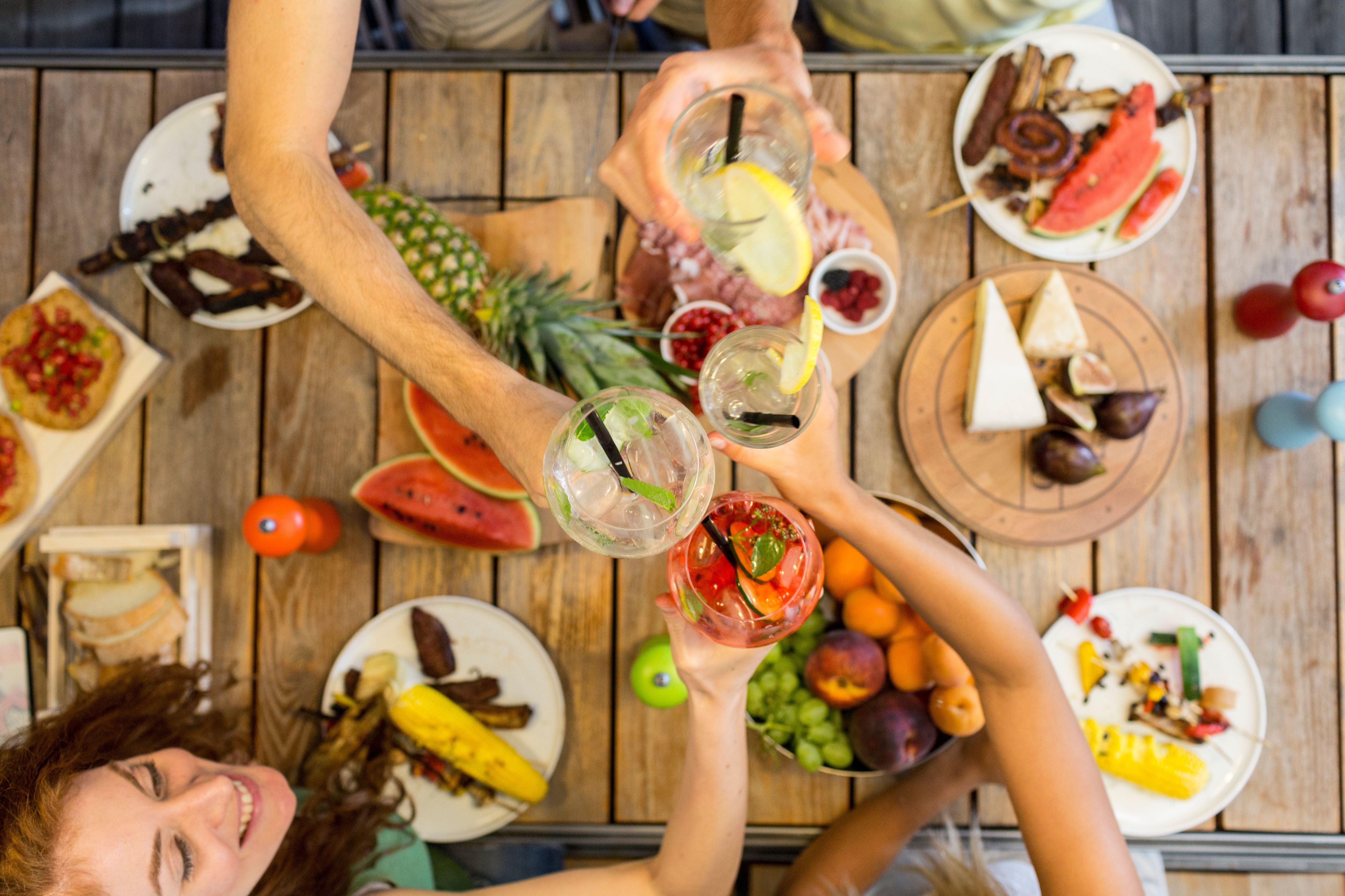 Draufsicht auf Sommersnacks und vier Menschen, die mit Getränken anstoßen.