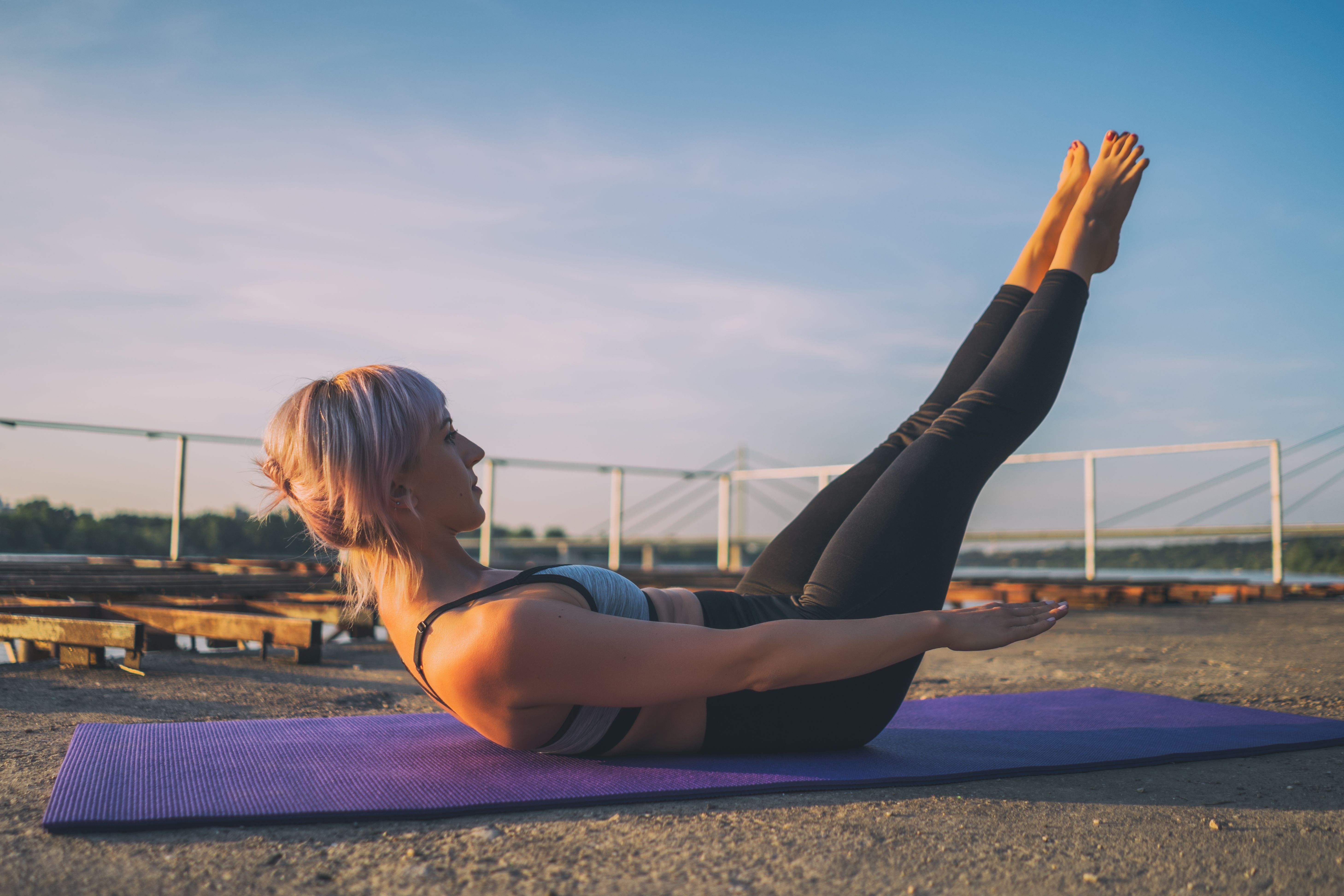 Frau macht Pilates-Hundert-Übung auf lila Matte im Freien bei Sonnenschein.
