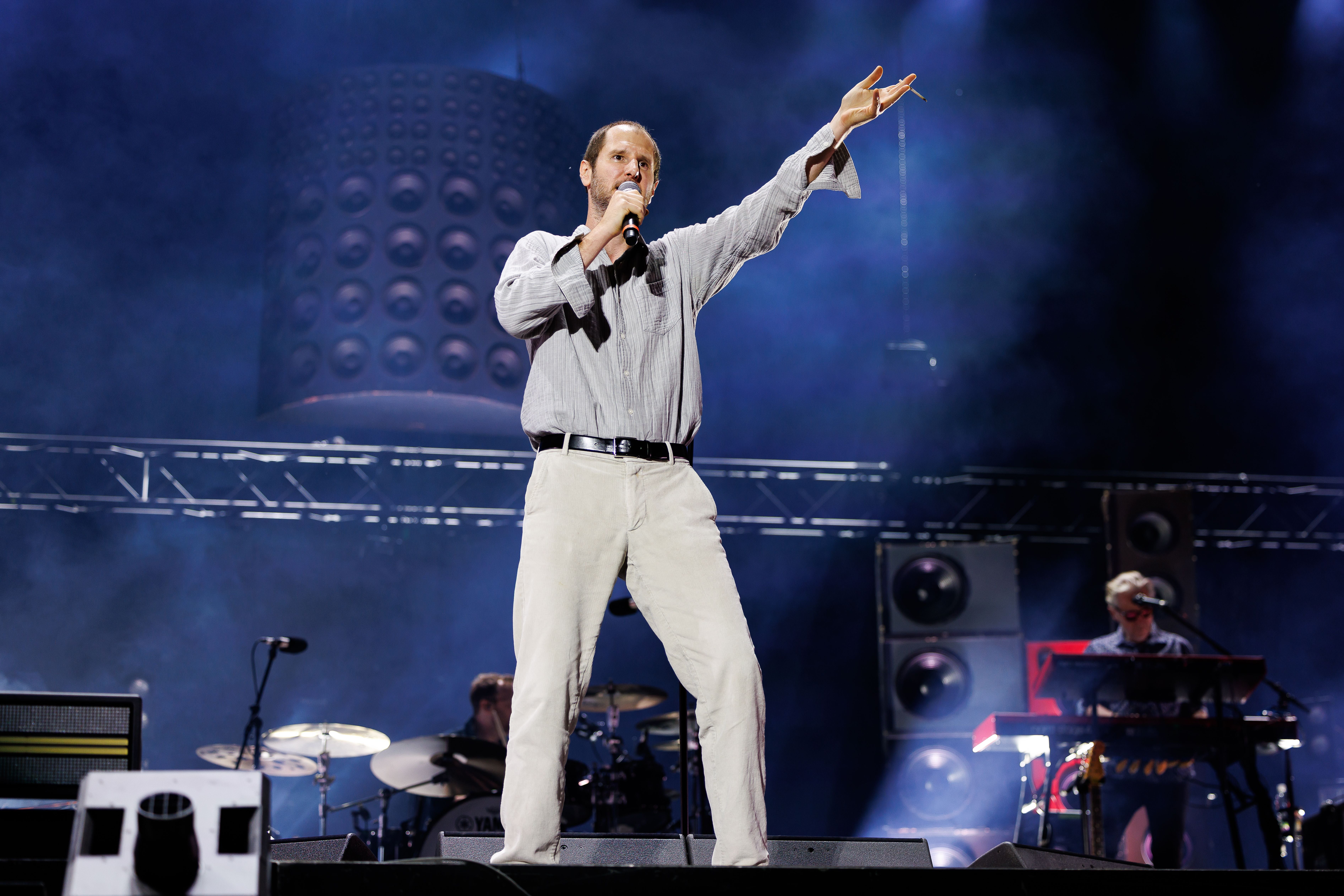 Ein Sänger mit Mikrofon performt auf einer großen Festivalbühne im Scheinwerferlicht.