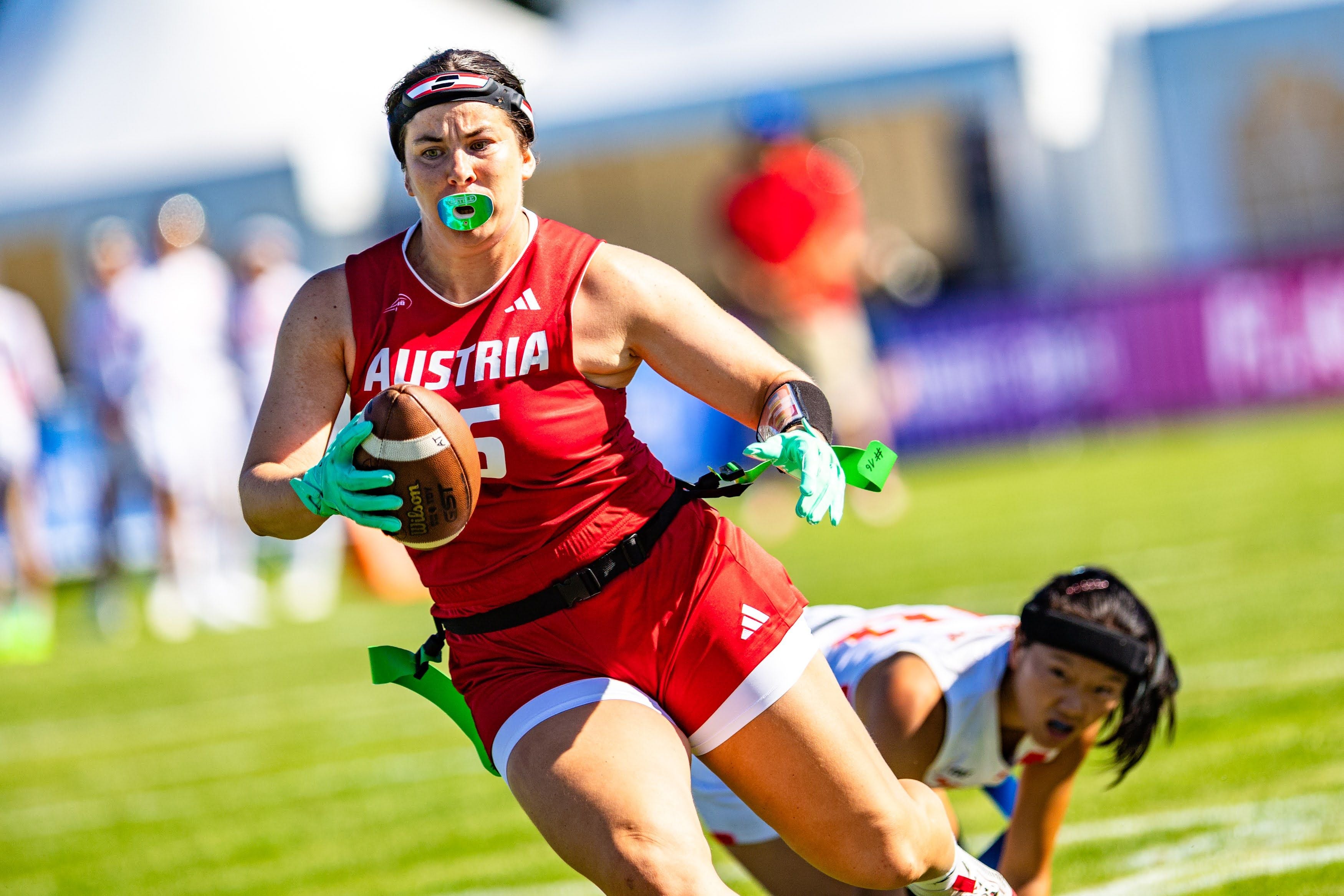 Eine österreichische Flag-Football-Spielerin läuft mit dem Ball, eine chinesische Gegnerin am Boden.