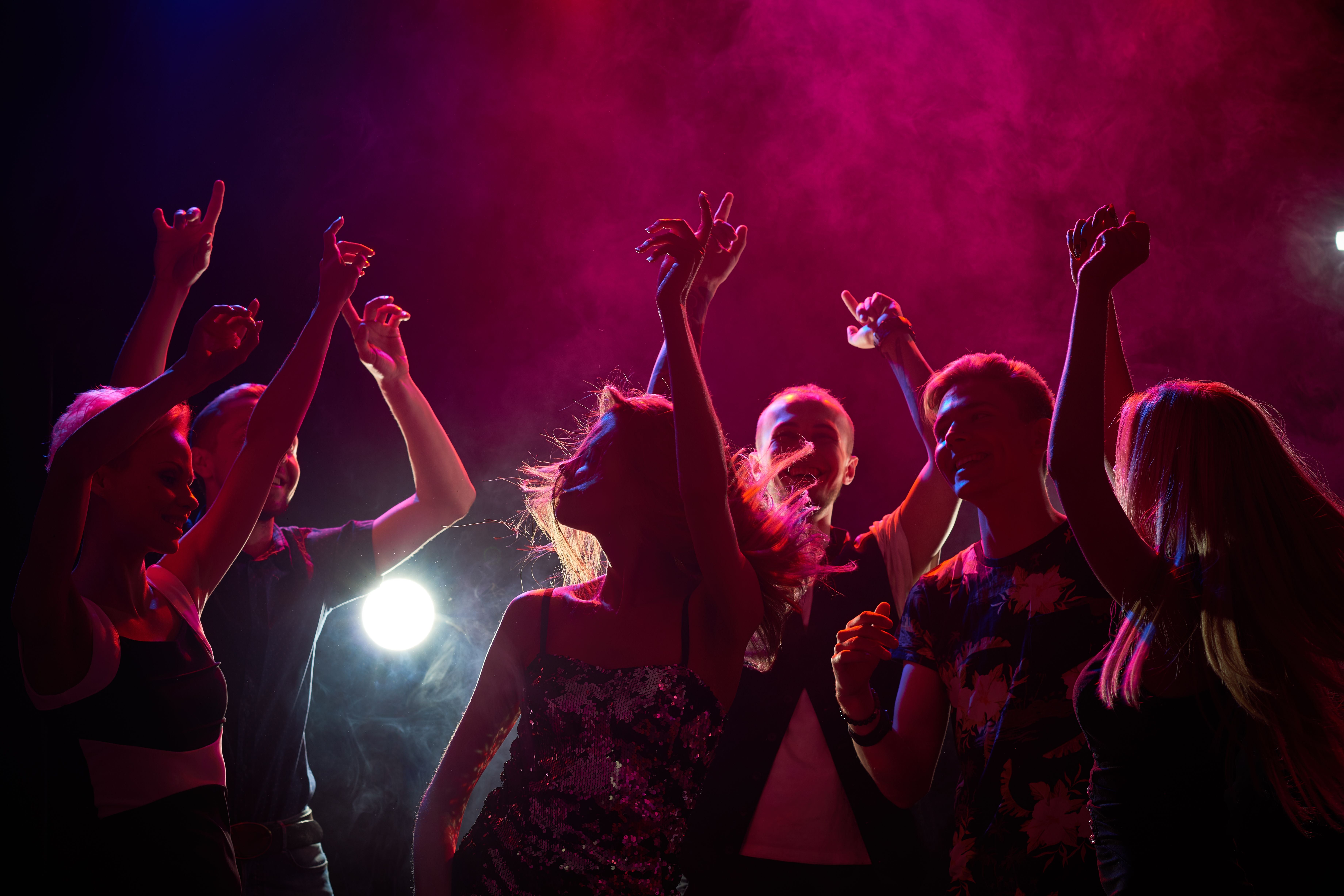 Mehrere Jugendliche tanzen und feiern ausgelassen in einem Nachtclub mit buntem Licht.