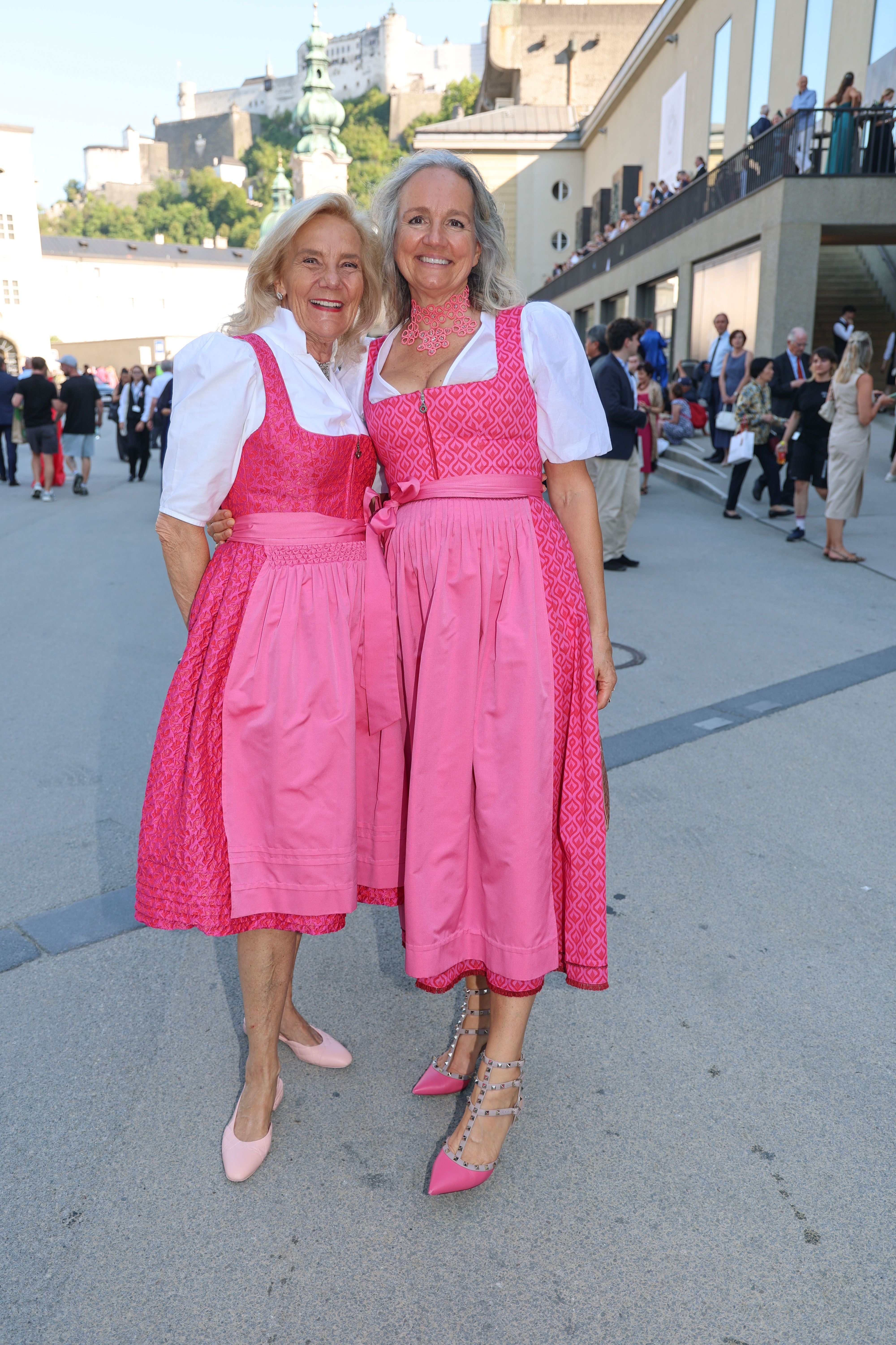 Zwei Frauen in rosa Dirndlkleidern lächeln auf einer Straße bei den Salzburger Festspielen.