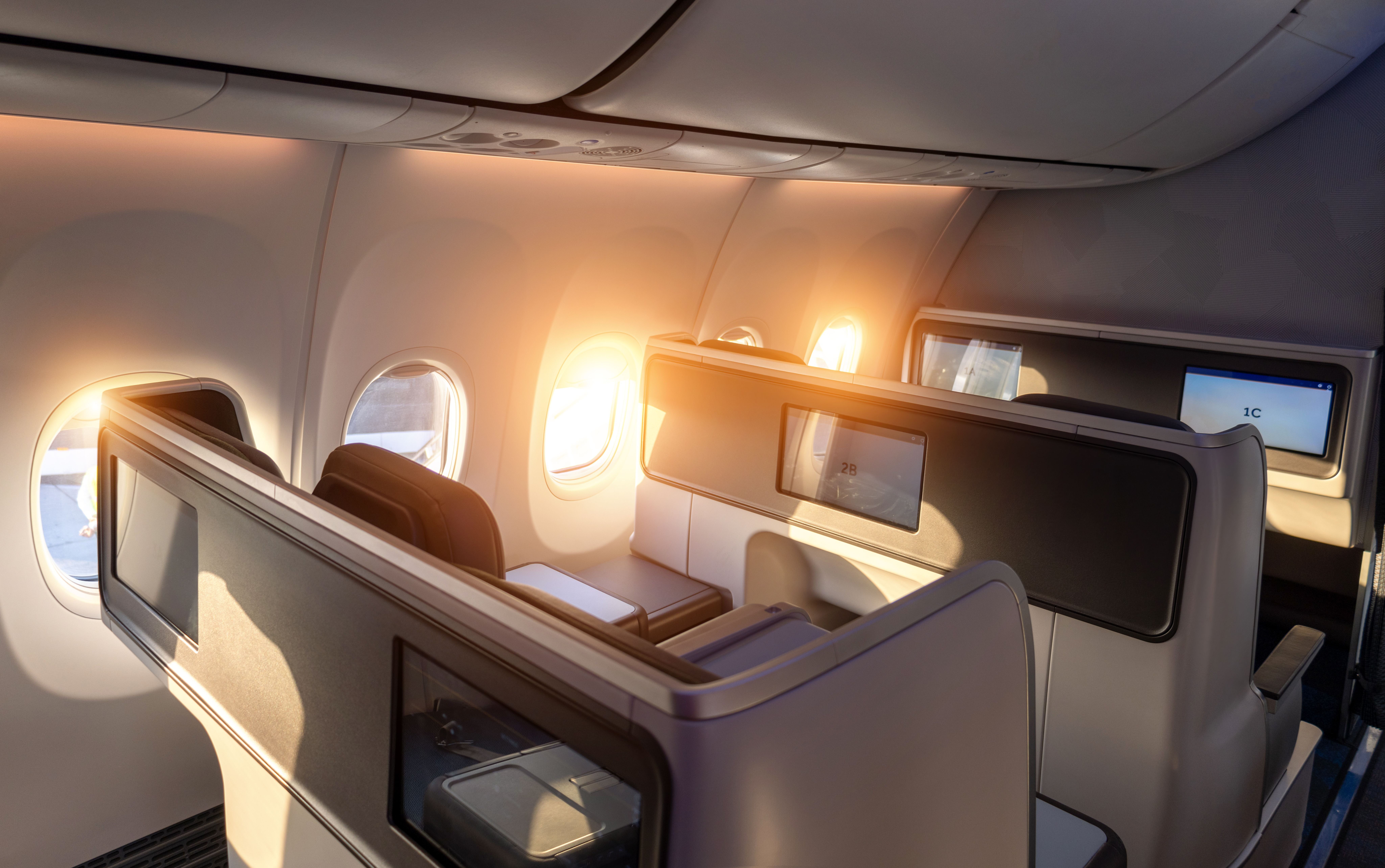 Moderne Flugzeugkabine mit luxuriösen First- und Business-Class-Sitzen bei Sonnenlicht.