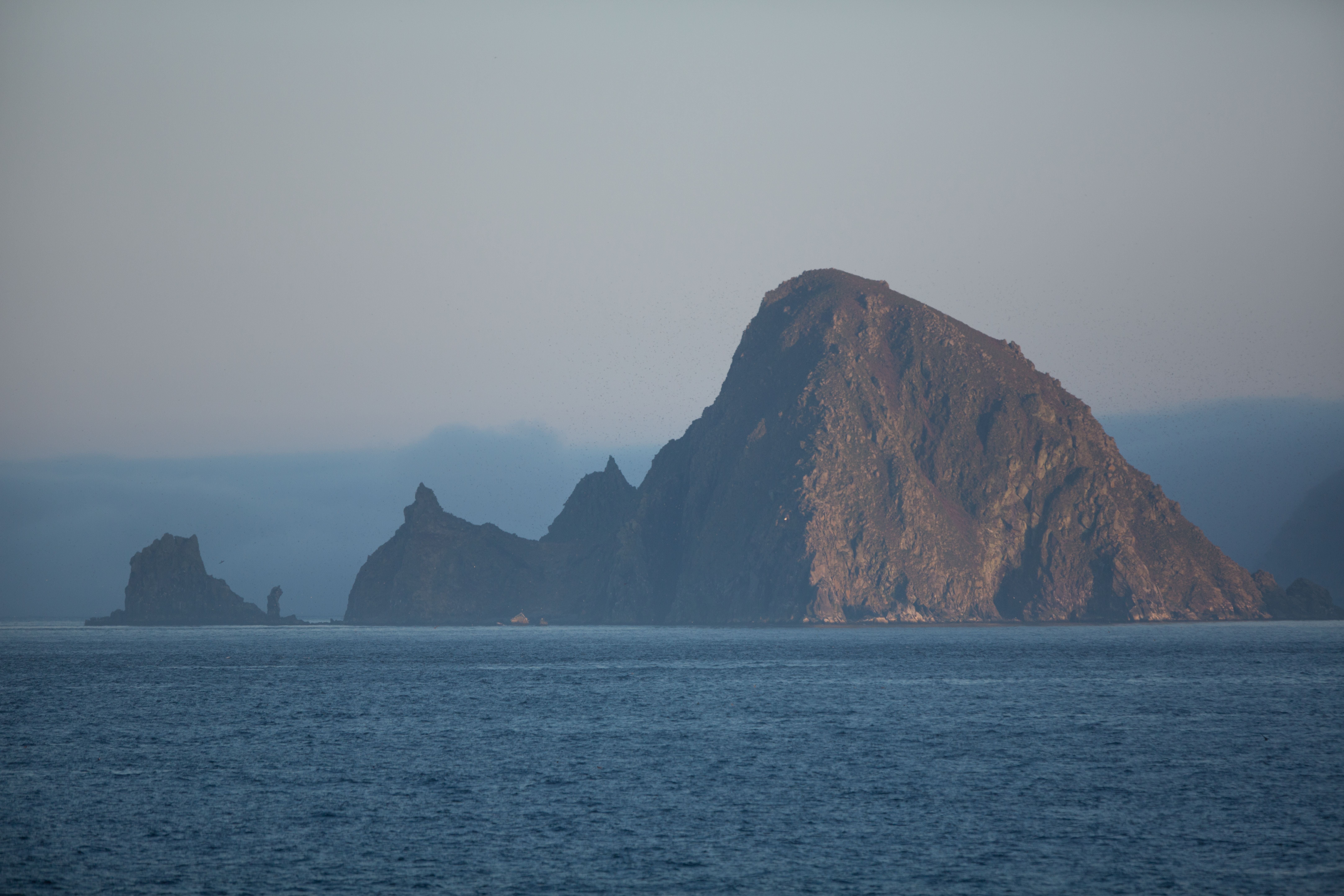 Felsige Insel Chirpoy im Meer bei ruhiger See und leicht bewölktem Himmel.