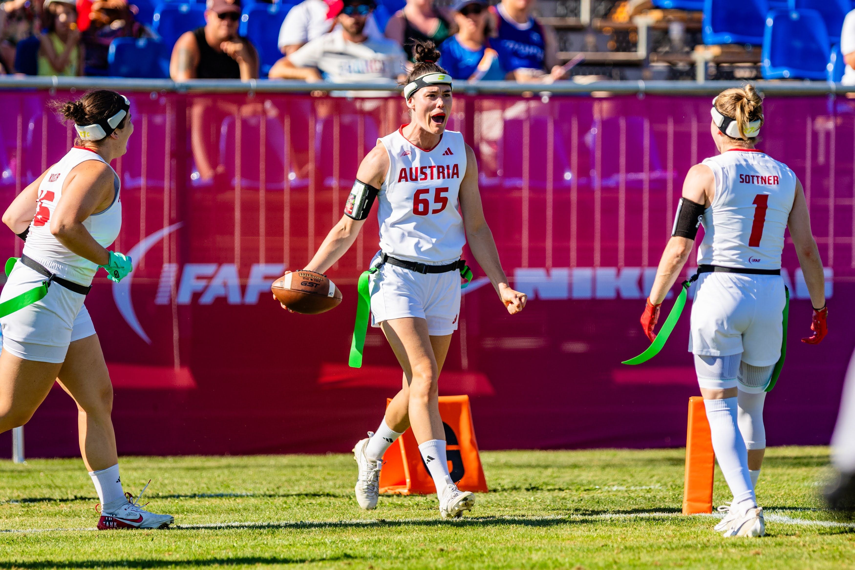 Drei österreichische Flag Football-Spielerinnen jubeln mit einem Football auf dem Spielfeld.