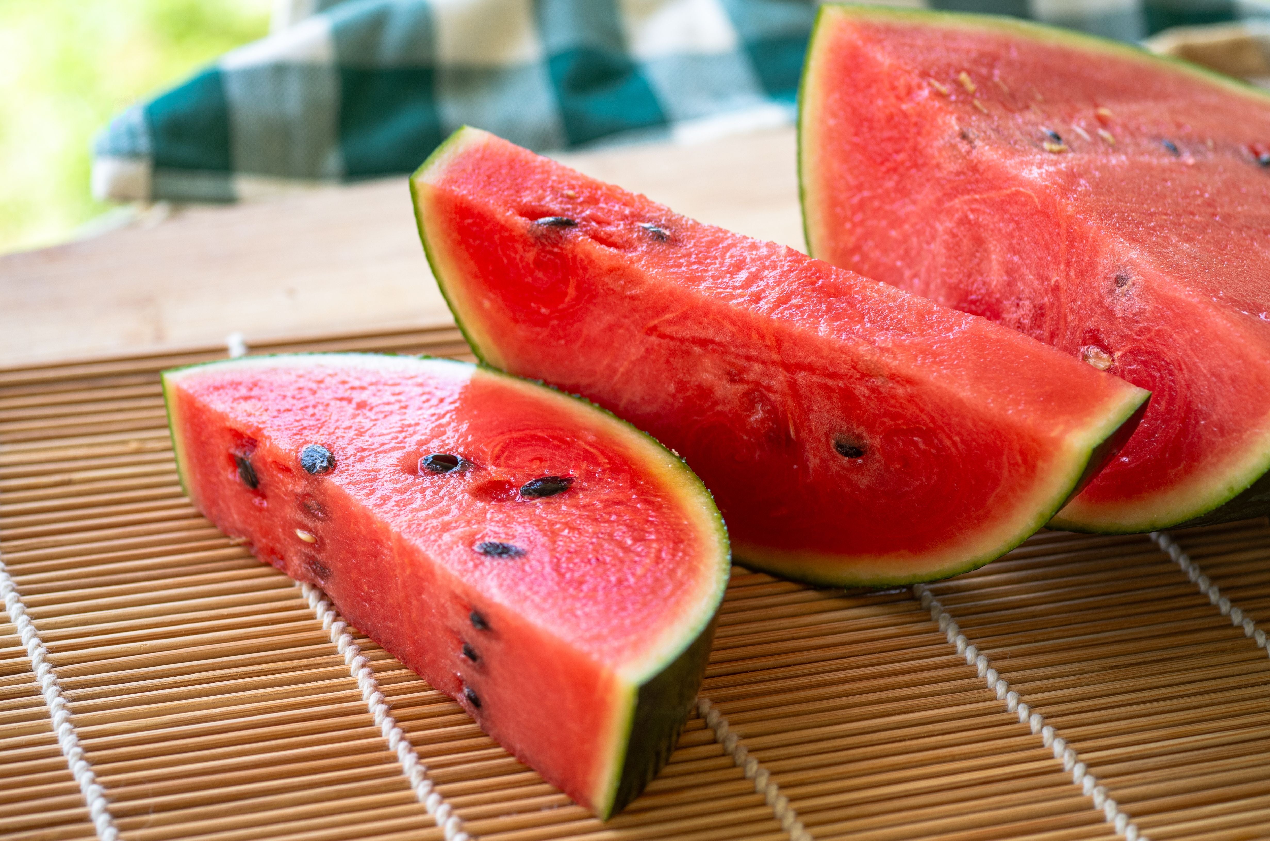 Drei frische Wassermelonenstücke liegen auf einer Bambusmatte.