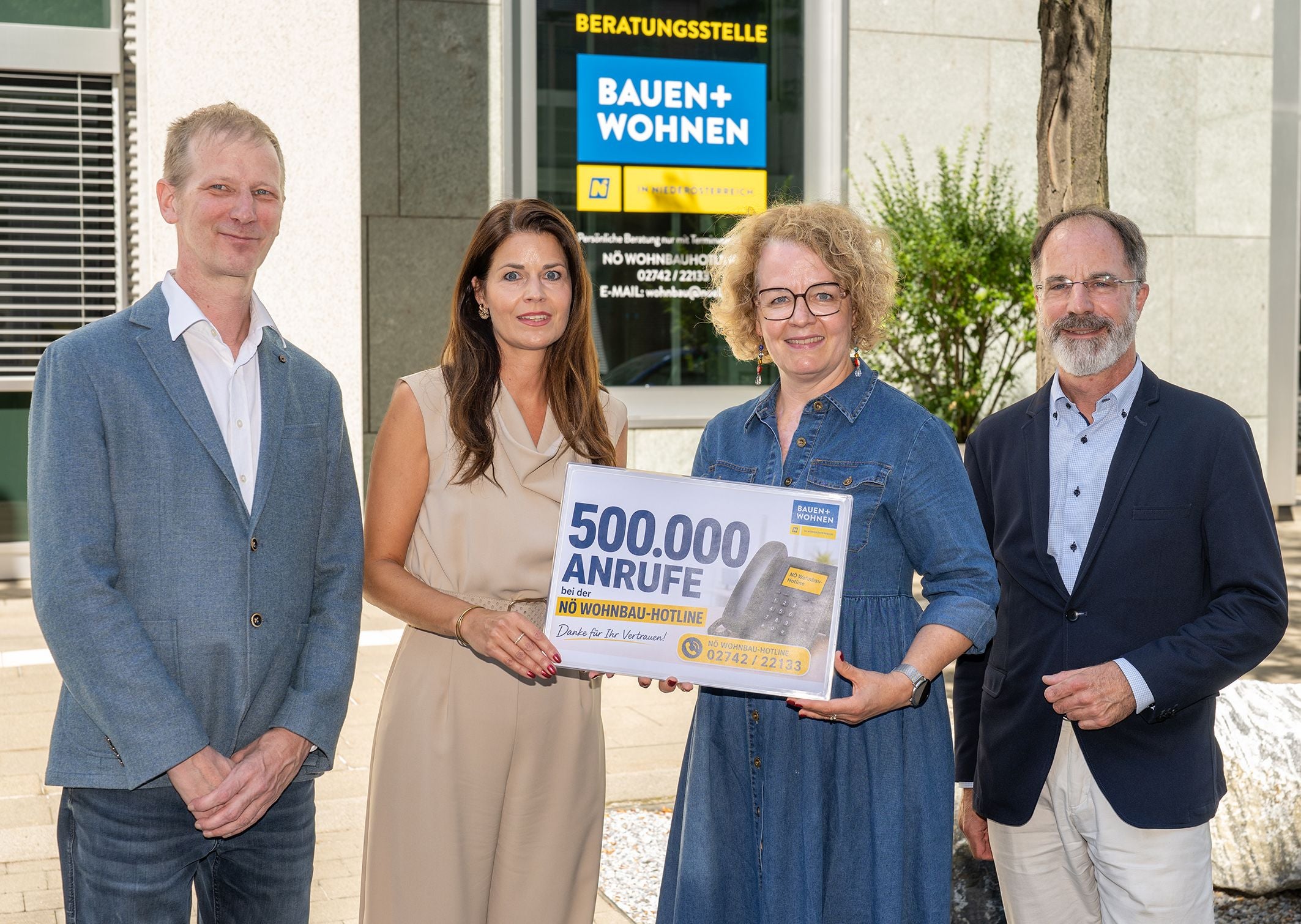 Vier Personen stehen vor einem Gebäude und halten ein Schild mit "500.000 Anrufe" in die Kamera.