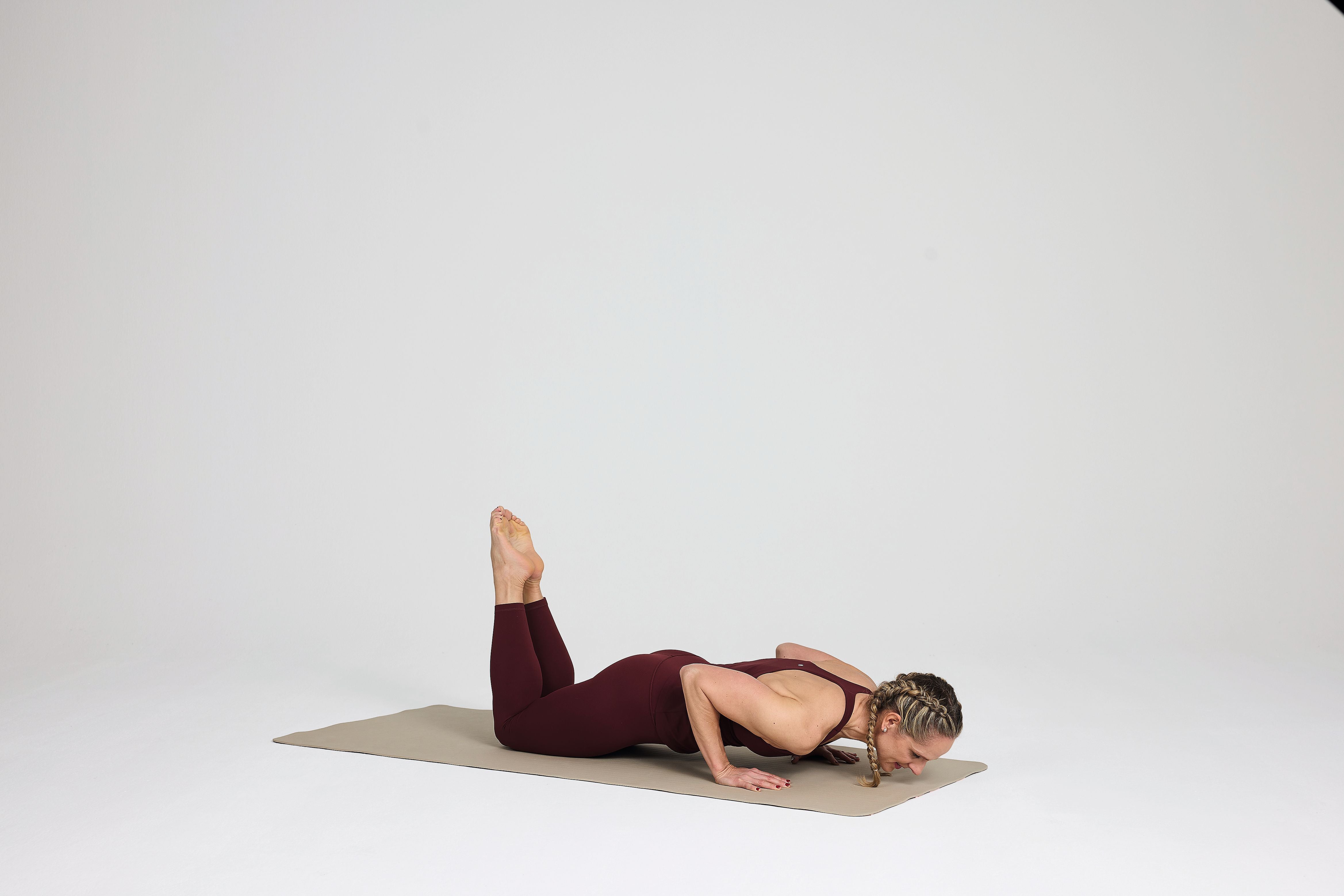 Frau macht Liegestütze auf Knien auf einer Yogamatte in einem leeren Raum.