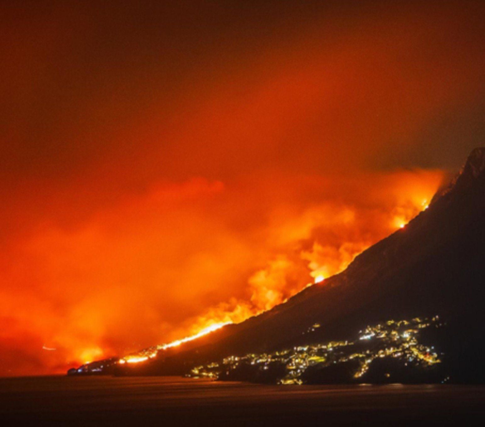 Großes Feuer am Berghang über einer kroatischen Stadt bei Nacht.
