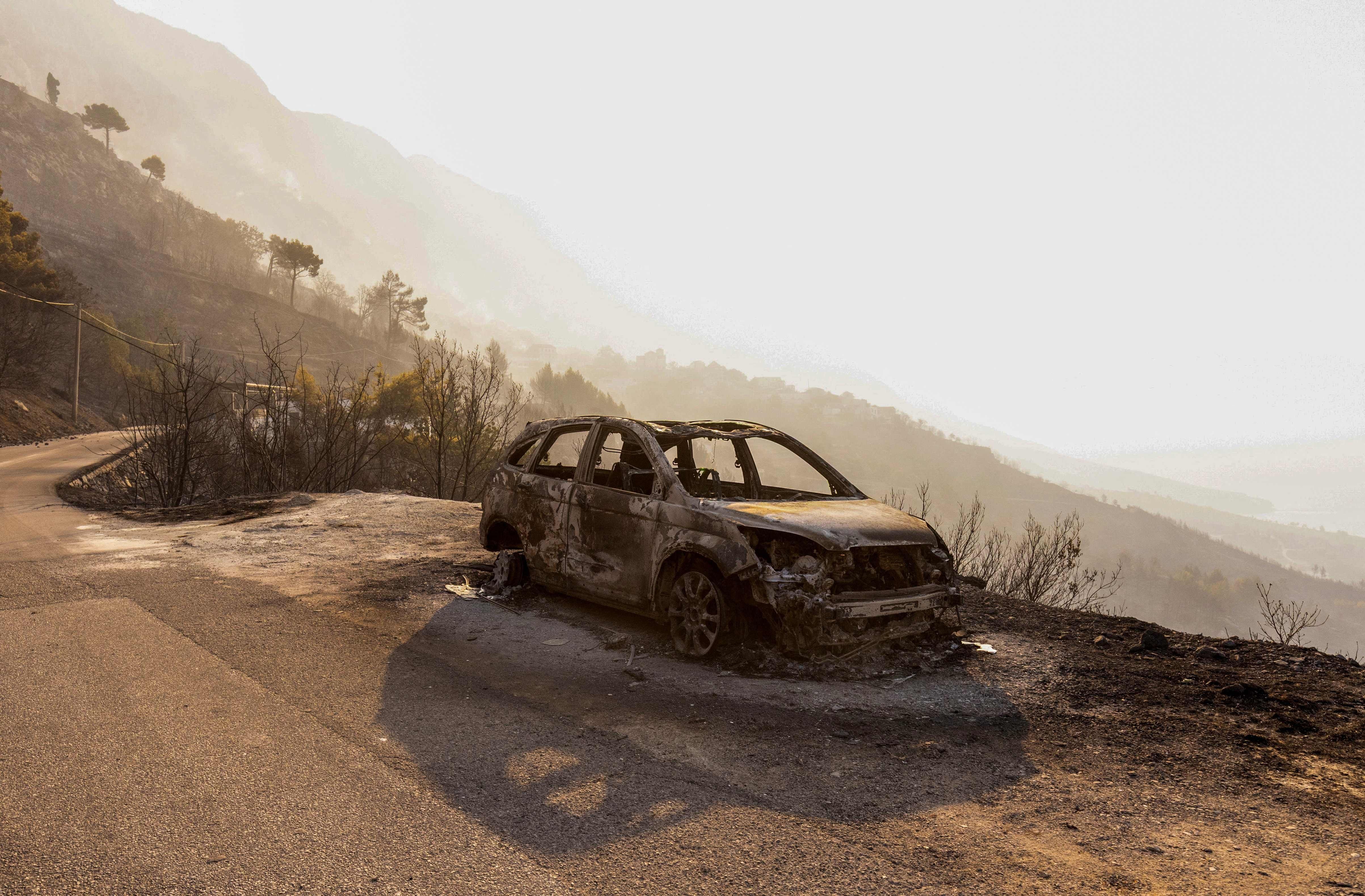 Ausgebranntes Auto steht nach einem Waldbrand auf einer Straße in hügeliger Landschaft bei Omis.