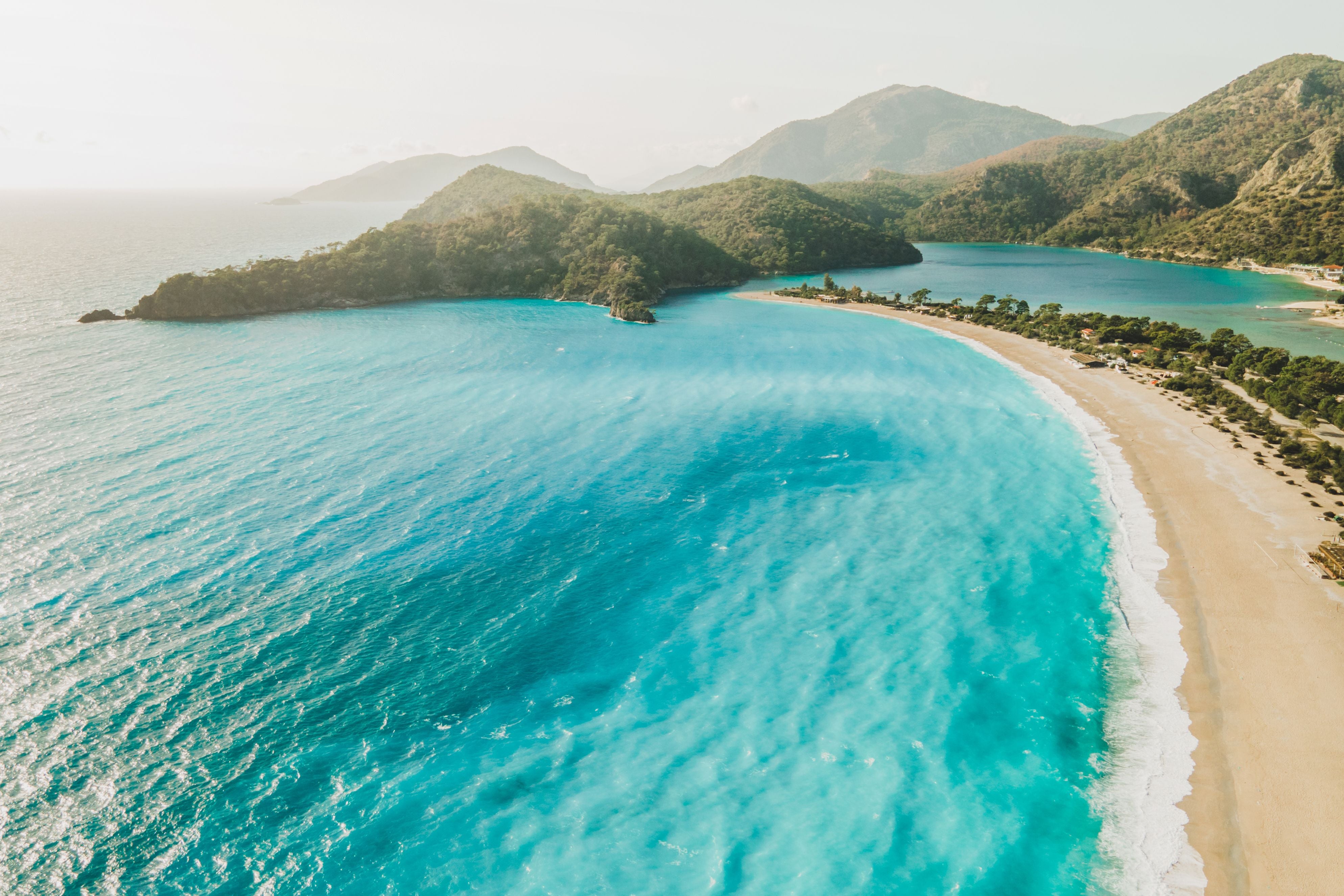Drohnenaufnahme von türkisblauem Meer, Sandstrand und grünen Bergen in der Türkei.