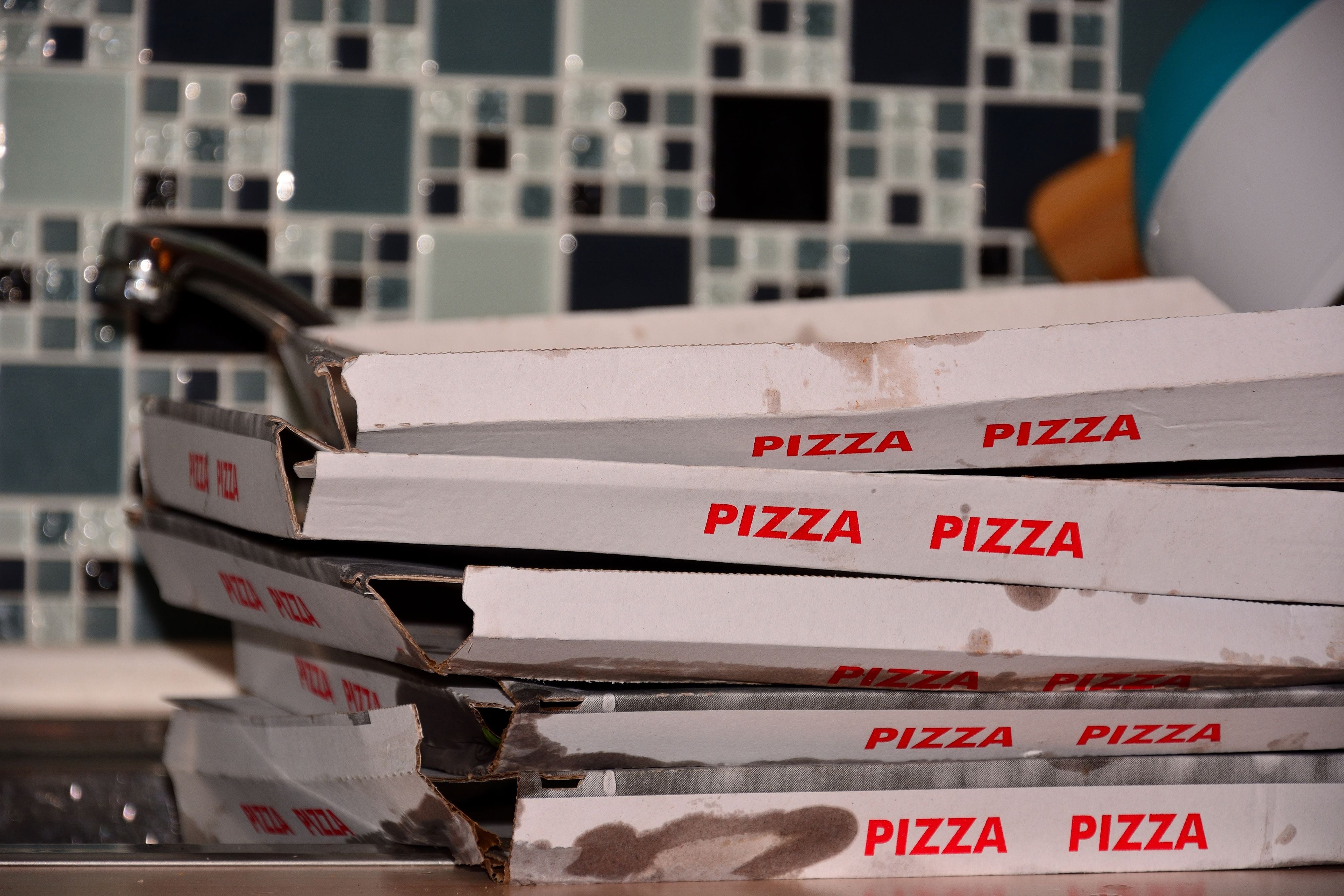 Fünf leere, schmutzige Pizzakartons liegen gestapelt auf einem Küchentisch.
