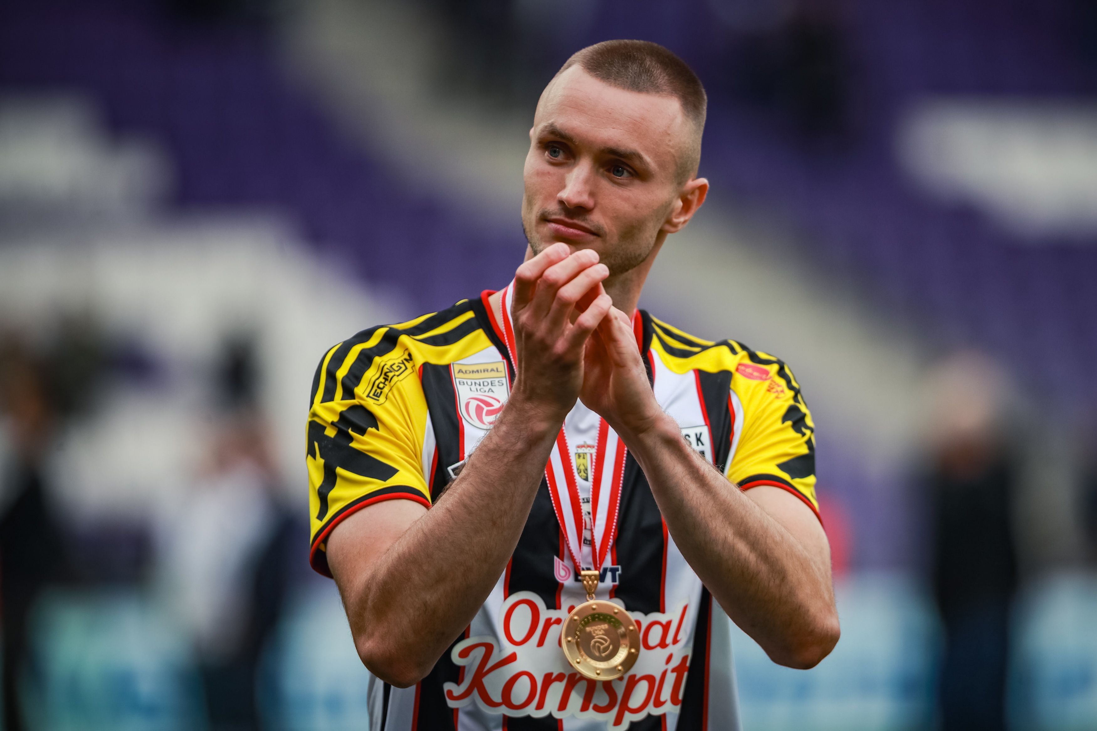 Ein Fußballspieler im LASK-Trikot mit Medaille klatscht und blickt zur Seite.