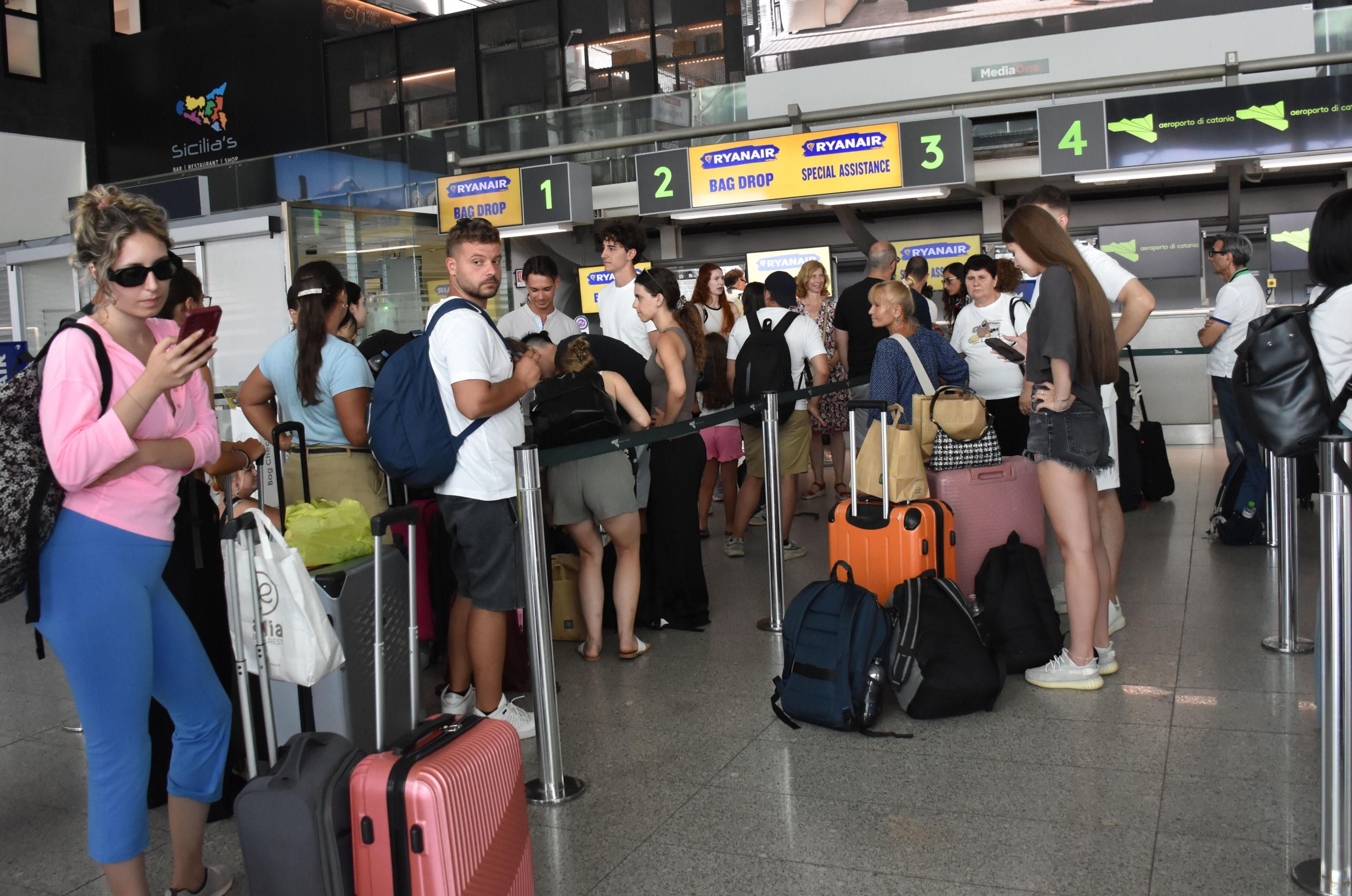 Reisende stehen mit Gepäck in einer Warteschlange am Flughafen Catania, Italien.
