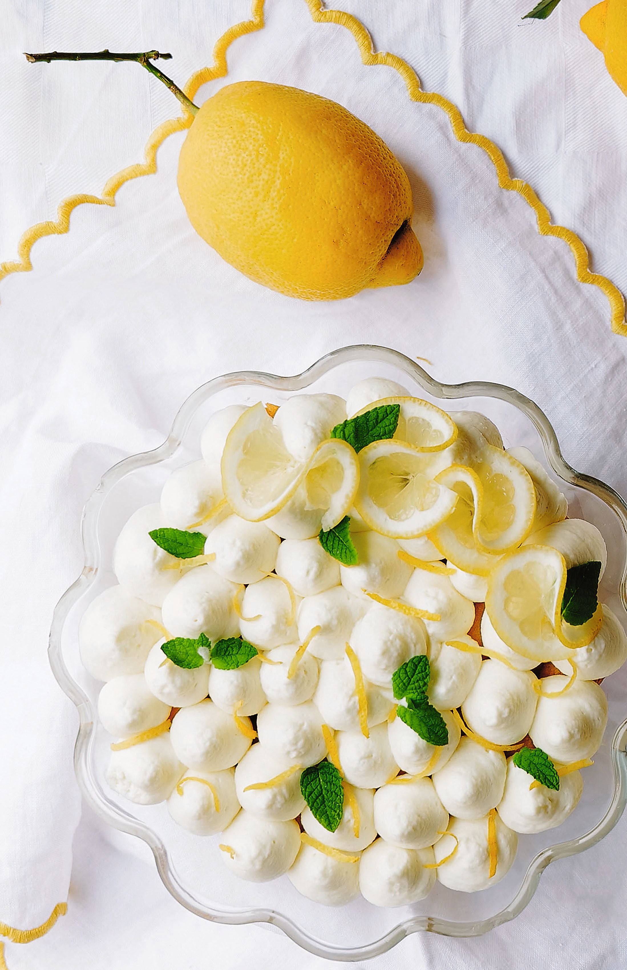 Zitronendessert mit Baiser, Zitronenscheiben und Minzblättern auf weißer Tischdecke.