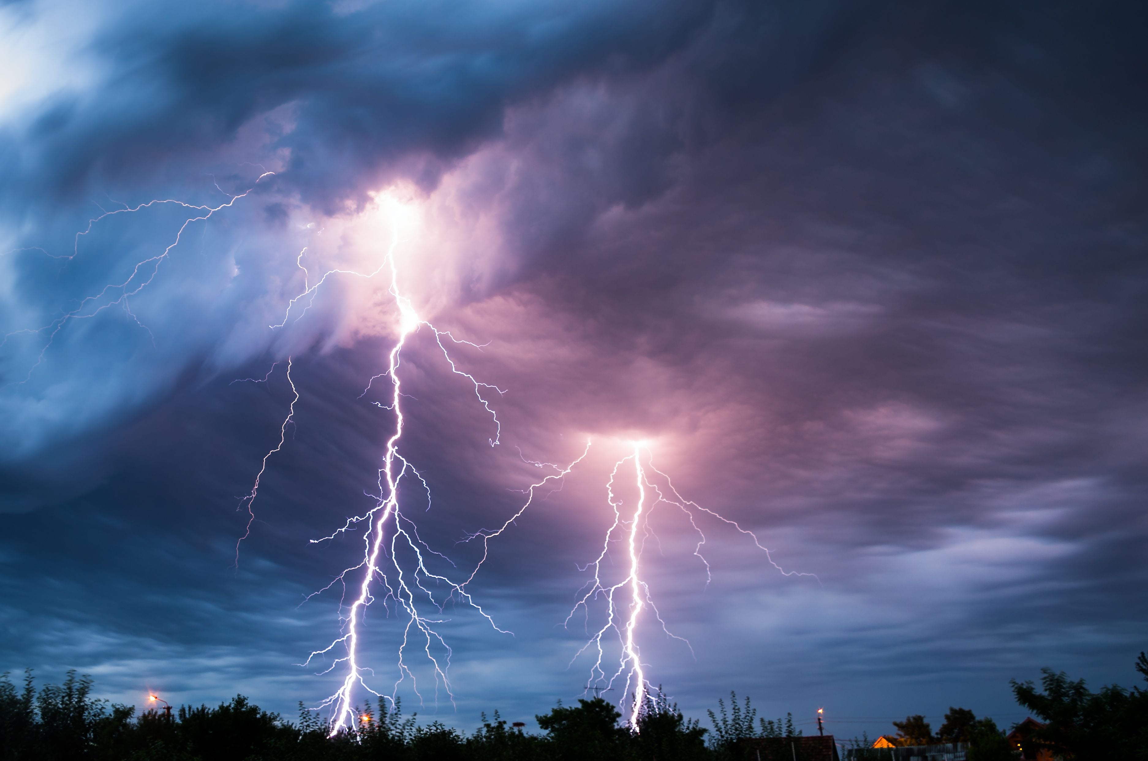 Blitze schlagen während eines Sturms aus dunklen Wolken über einer Landschaft ein.