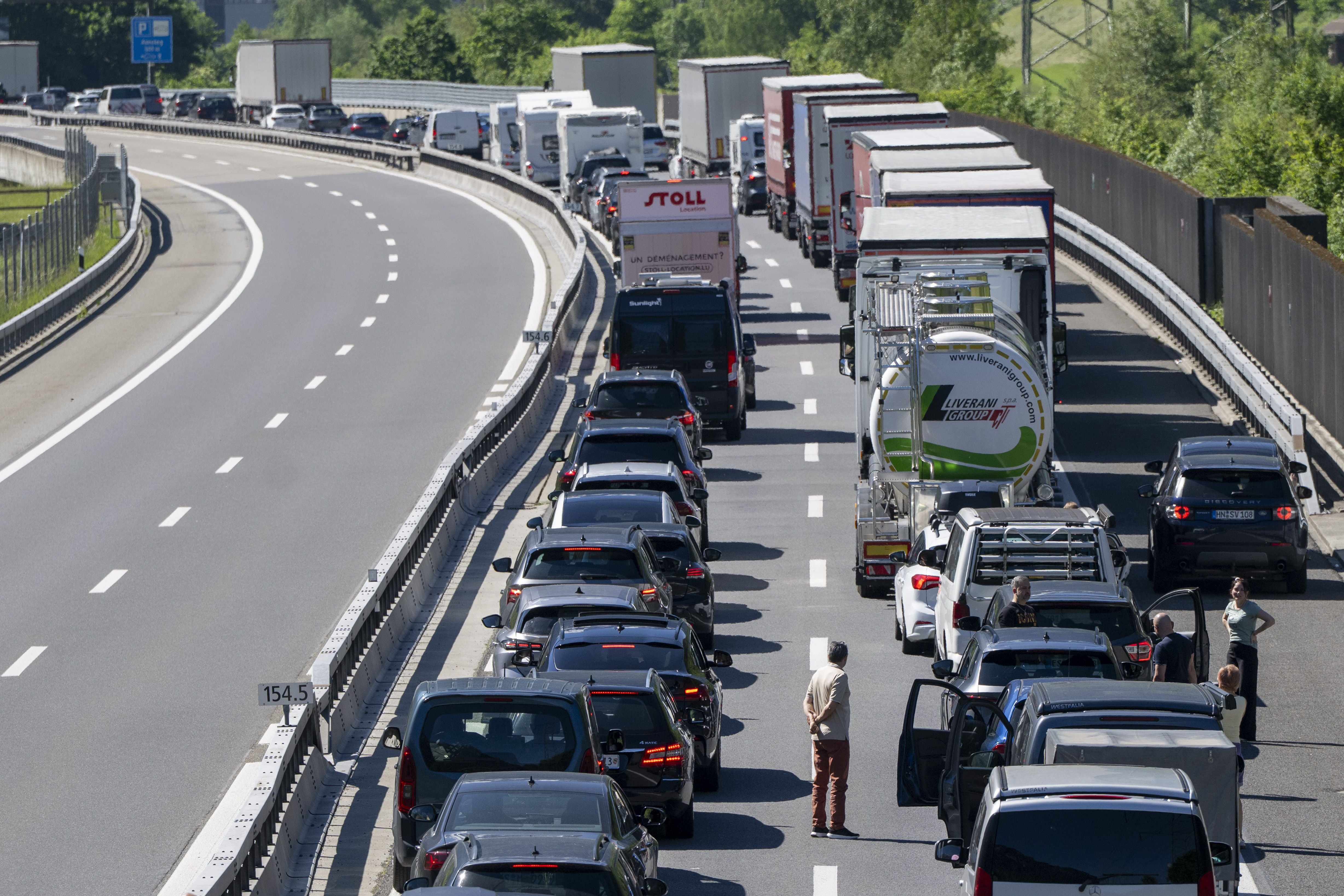 Langer Stau mit Autos und Lastwagen auf der A2 bei Amsteg, Menschen stehen neben ihren Fahrzeugen.