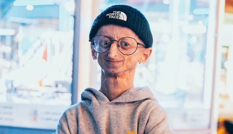 Eine Person mit Brille und Mütze lächelt, trägt einen grauen Hoodie.