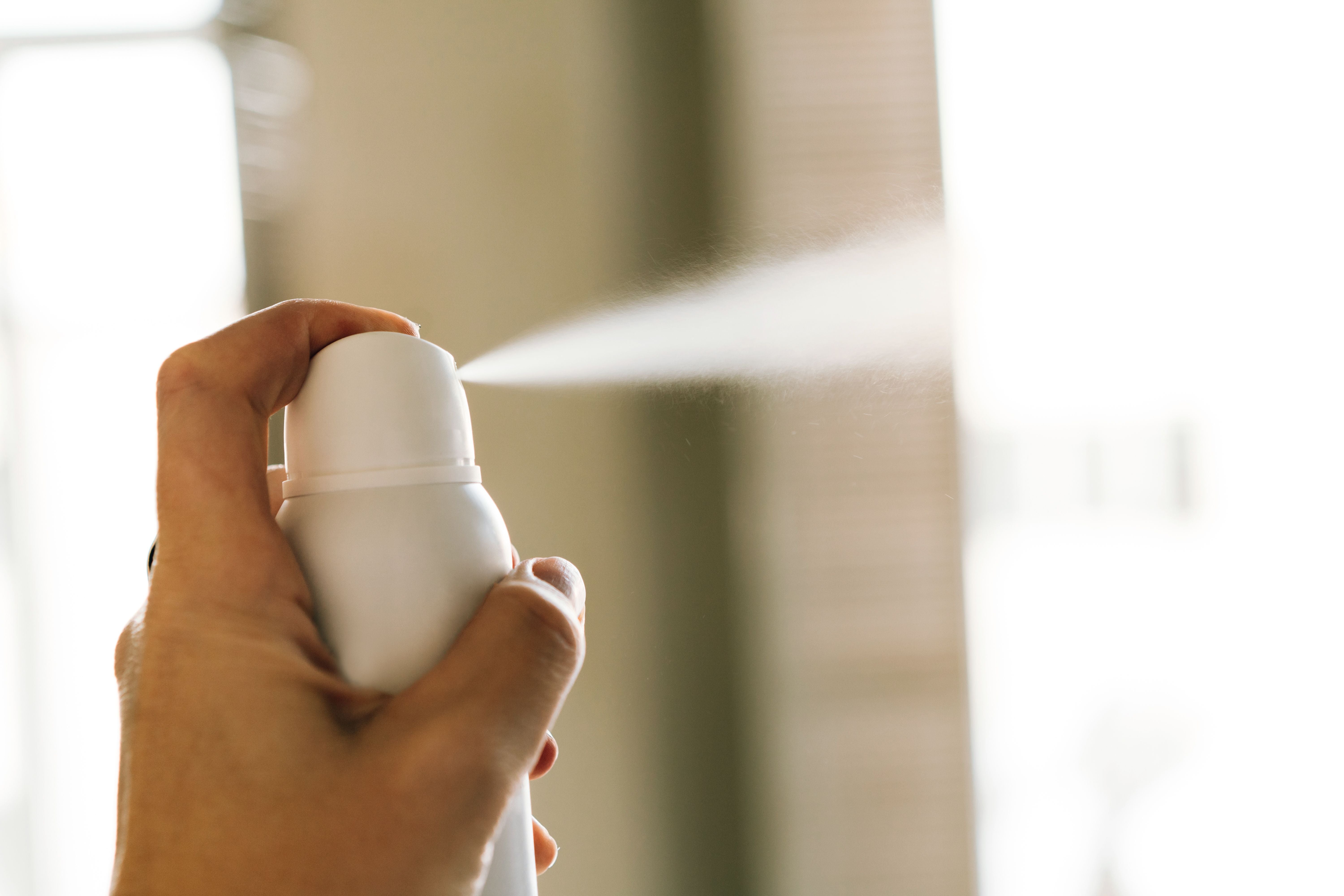 Eine Hand sprüht aus einer weißen Deodorantdose einen feinen Sprühnebel.